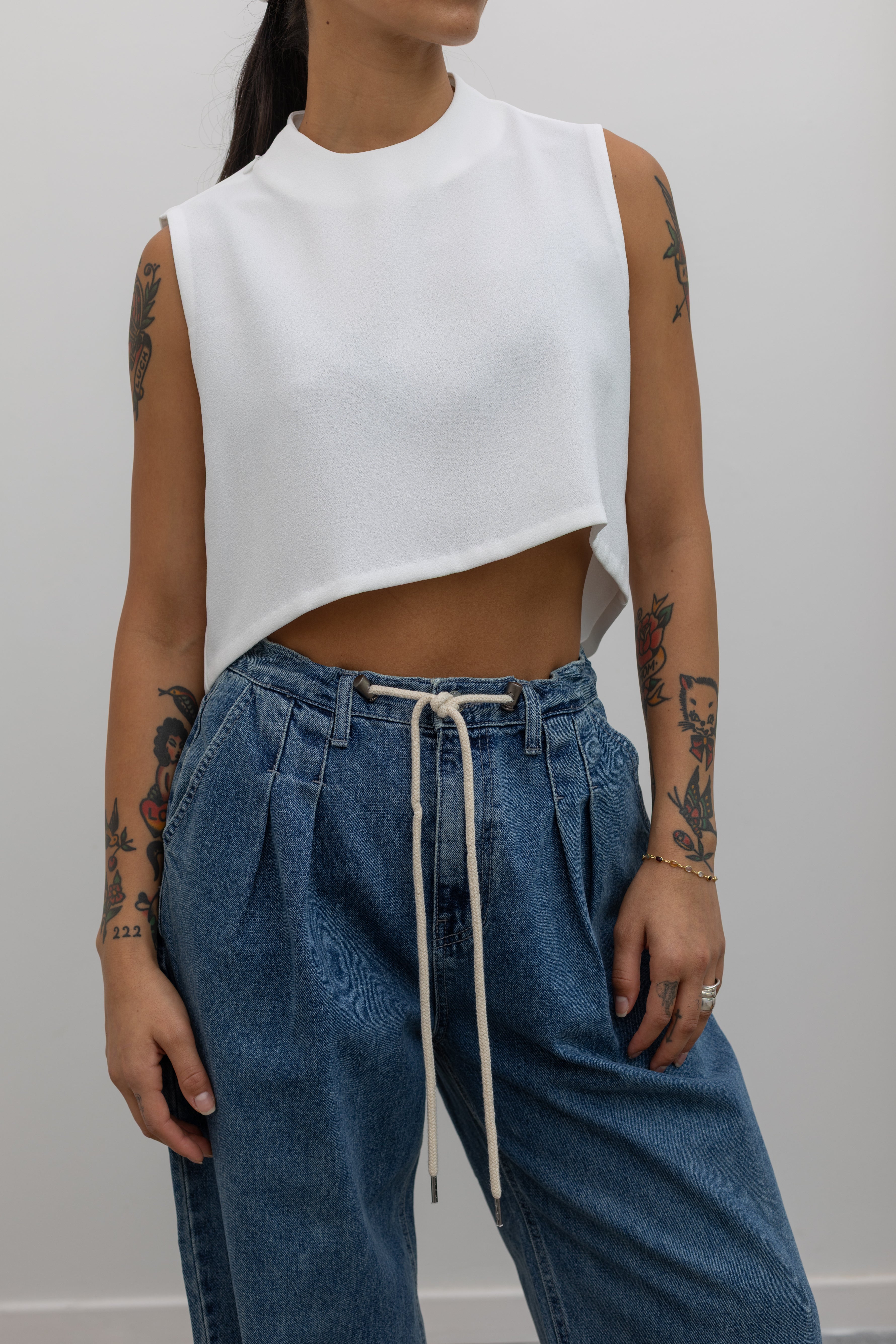 Close-up front view of a woman wearing capsule wardrobe essential style in a Kaarem White Raised Collar Wind Chime Cropped Top paired with light wash denim drawstring waist jeans at Alas Eius.