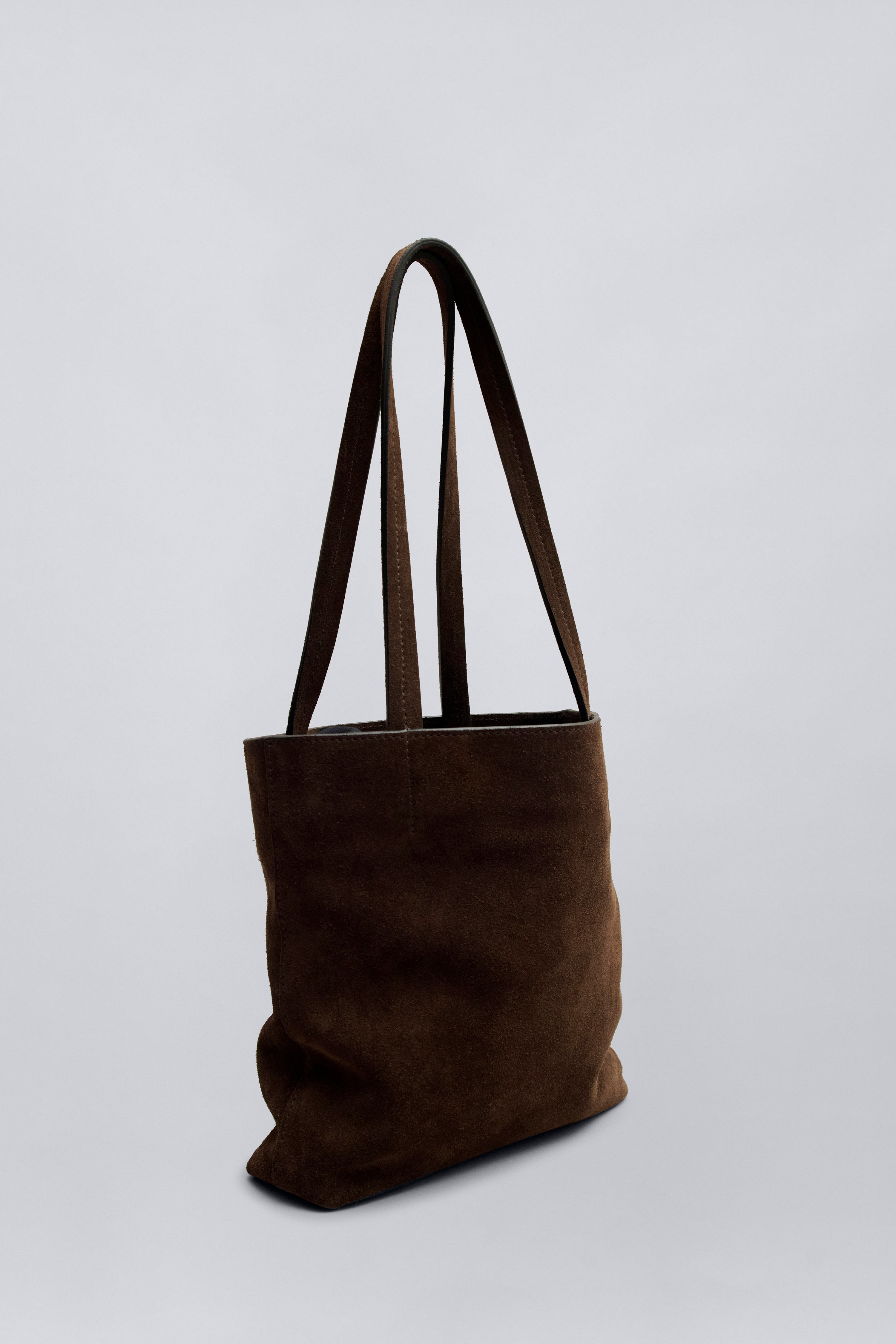 3/4 product view of a chic and elevated classic structured tote by Kallmeyer in rich brown suede, dual flat shoulder straps, and a permanent canvas drawstring pouch opening with leather toggles at Alas Eius. Made in Italy. 