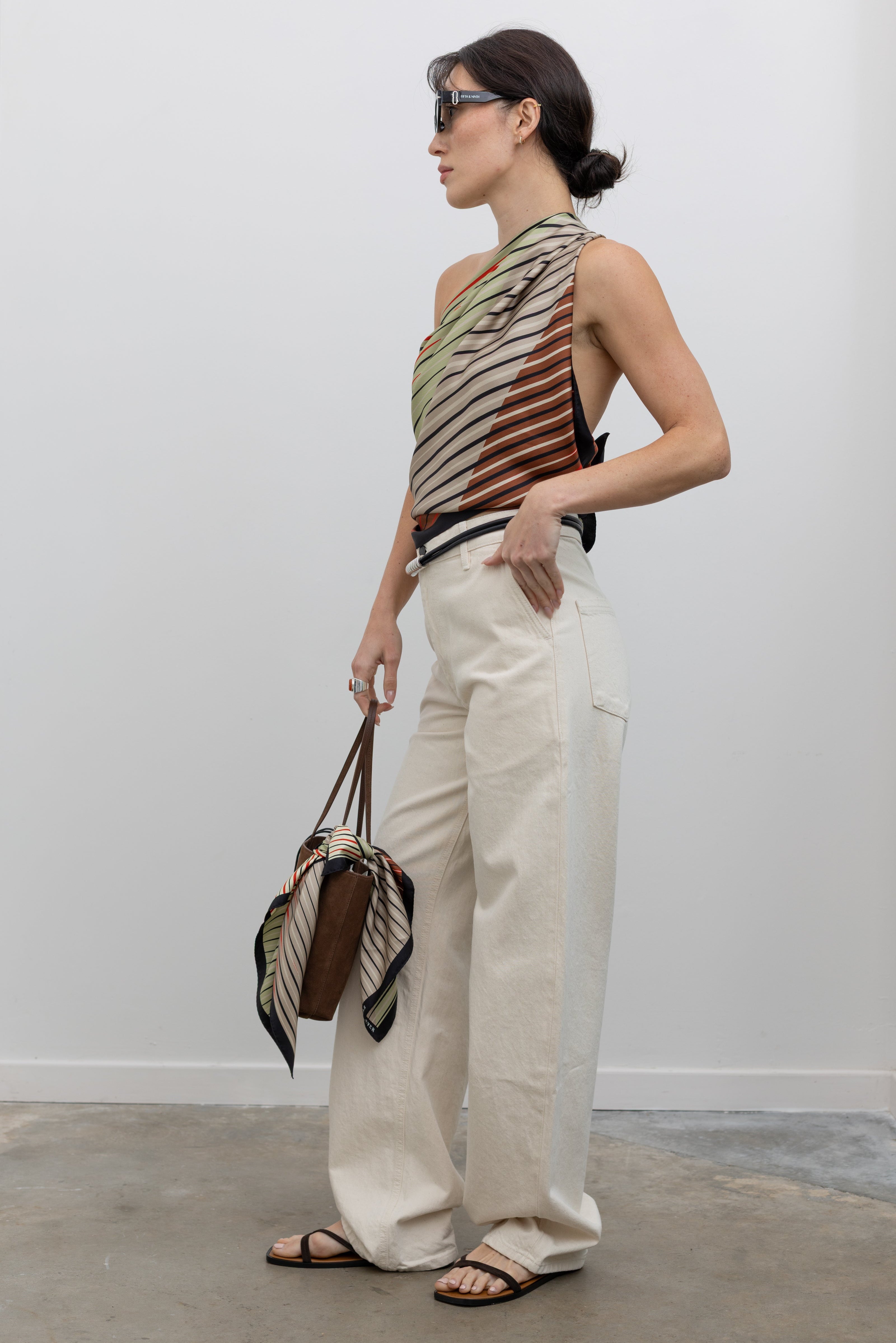 Full length 3/4 view of a woman wearing modern minimalist fashion in a Kallmeyer Neutral Silk Twill Fluted Scarf Top featuring a gradient stripe print, soft cowl neckline, and a deep open back paired with Kallmeyer Ecru Column Wide Leg Denim Jeans featuring a Mid-high rise, relaxed hip and thigh at an Alas Eius store. Made in Portugal. 