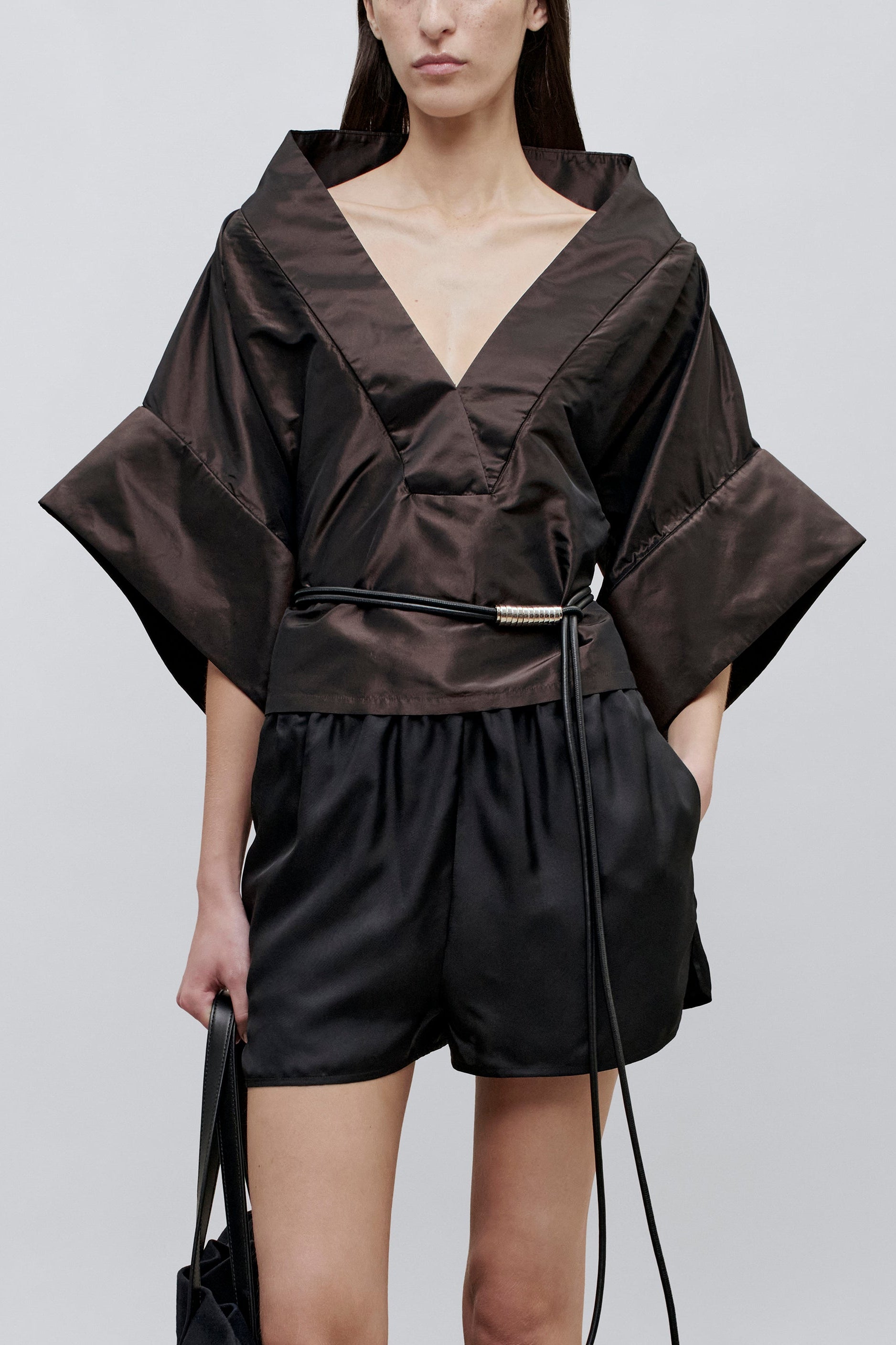 Front view of a woman wearing chic and contemporary fashion in a Kallmeyer Espresso Silk Taffeta Winslow Top featuring a crisp silk taffeta with dramatic structured v-neckline and oversized cuffed tunic sleeves at Alas Eius. Made in New York.