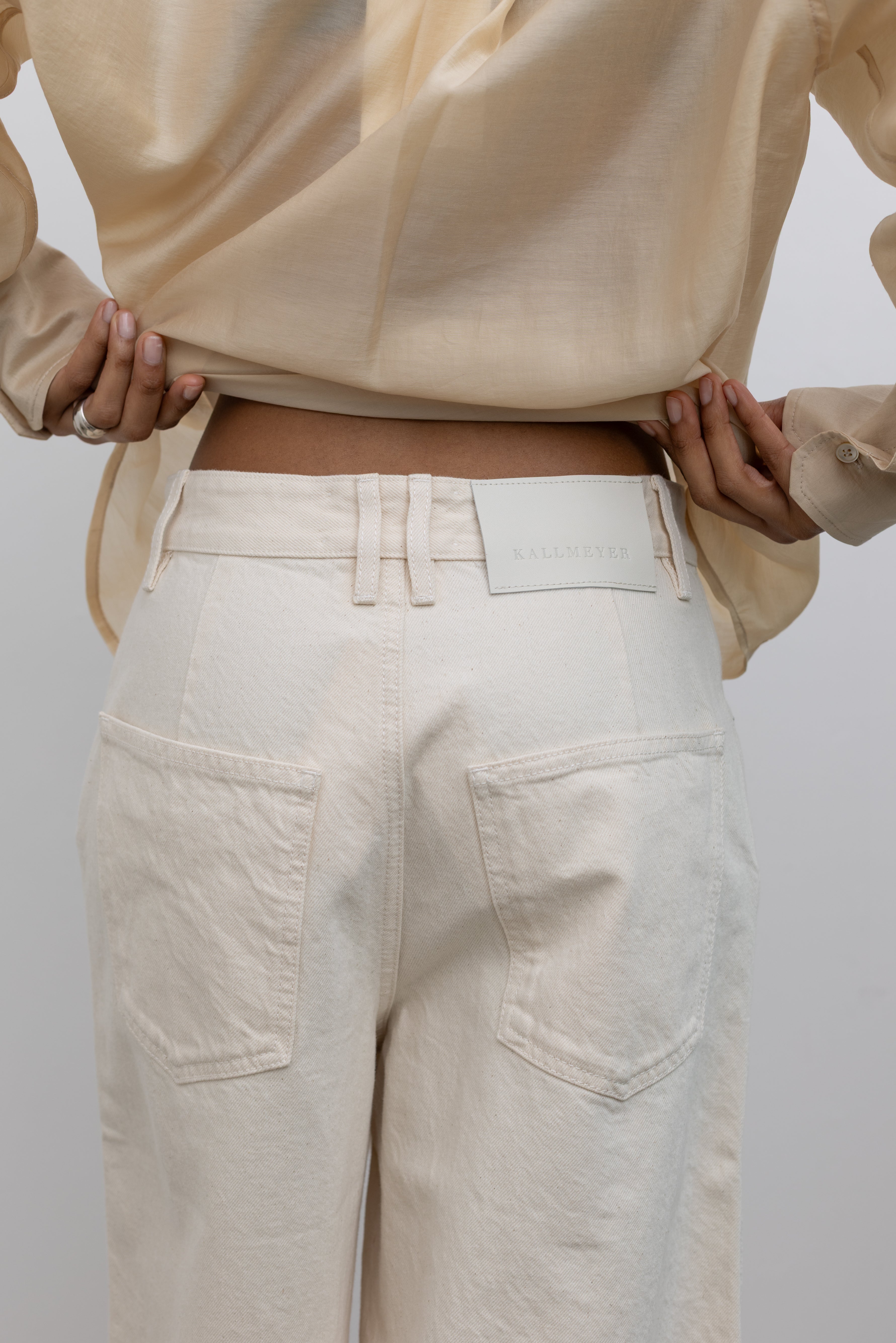 Close-up back view of a woman  wearing an elevated and modern take on a classic in a pair of Kallmeyer ecru cotton Hayes wide-leg denim shorts with a structured leg that stops just below the knee at an Alas Eius store. Made in Portugal.