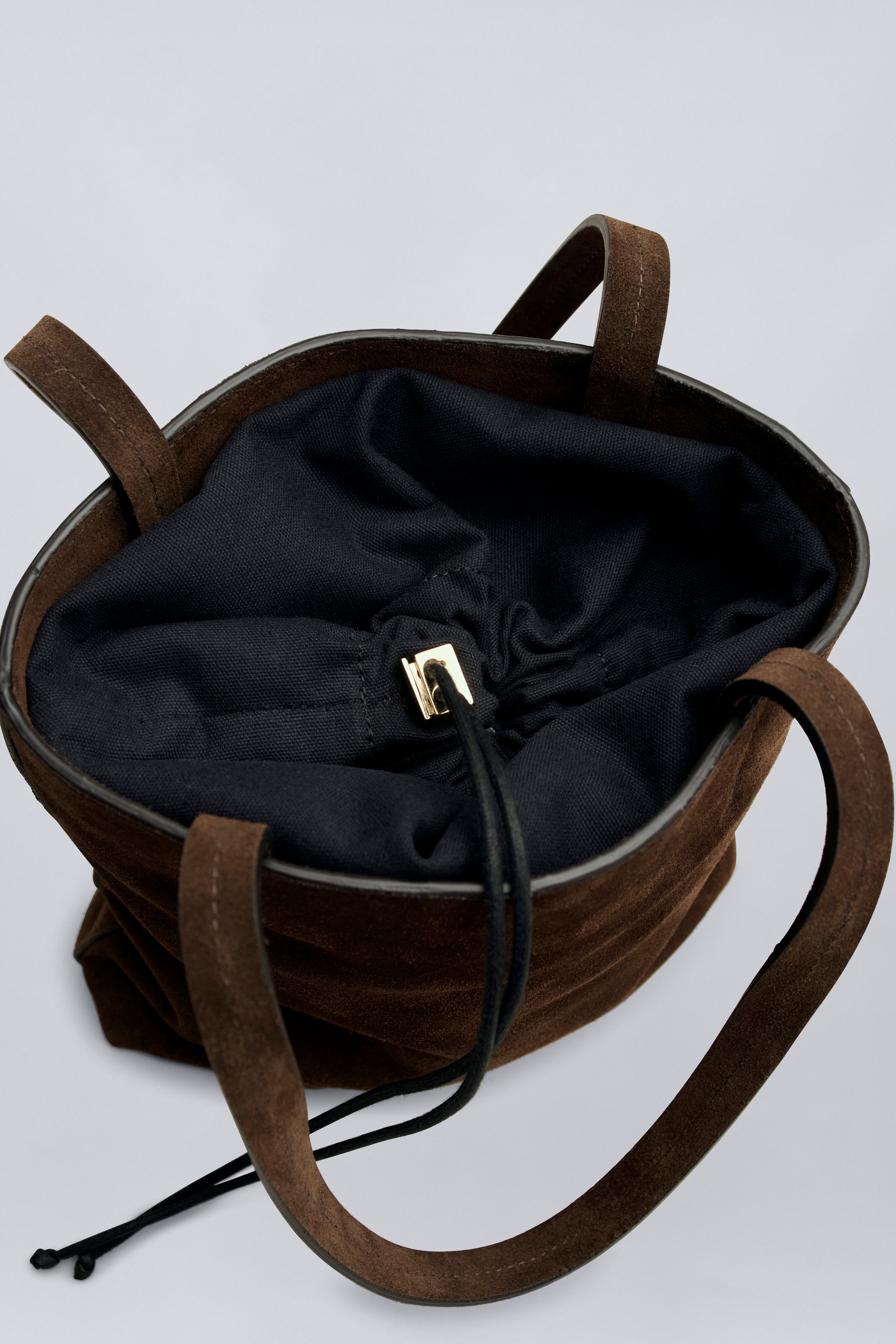 Aerial product view of a chic and elevated classic structured tote by Kallmeyer in rich brown suede, dual flat shoulder straps, and a permanent canvas drawstring pouch opening with leather toggles at Alas Eius. Made in Italy. 