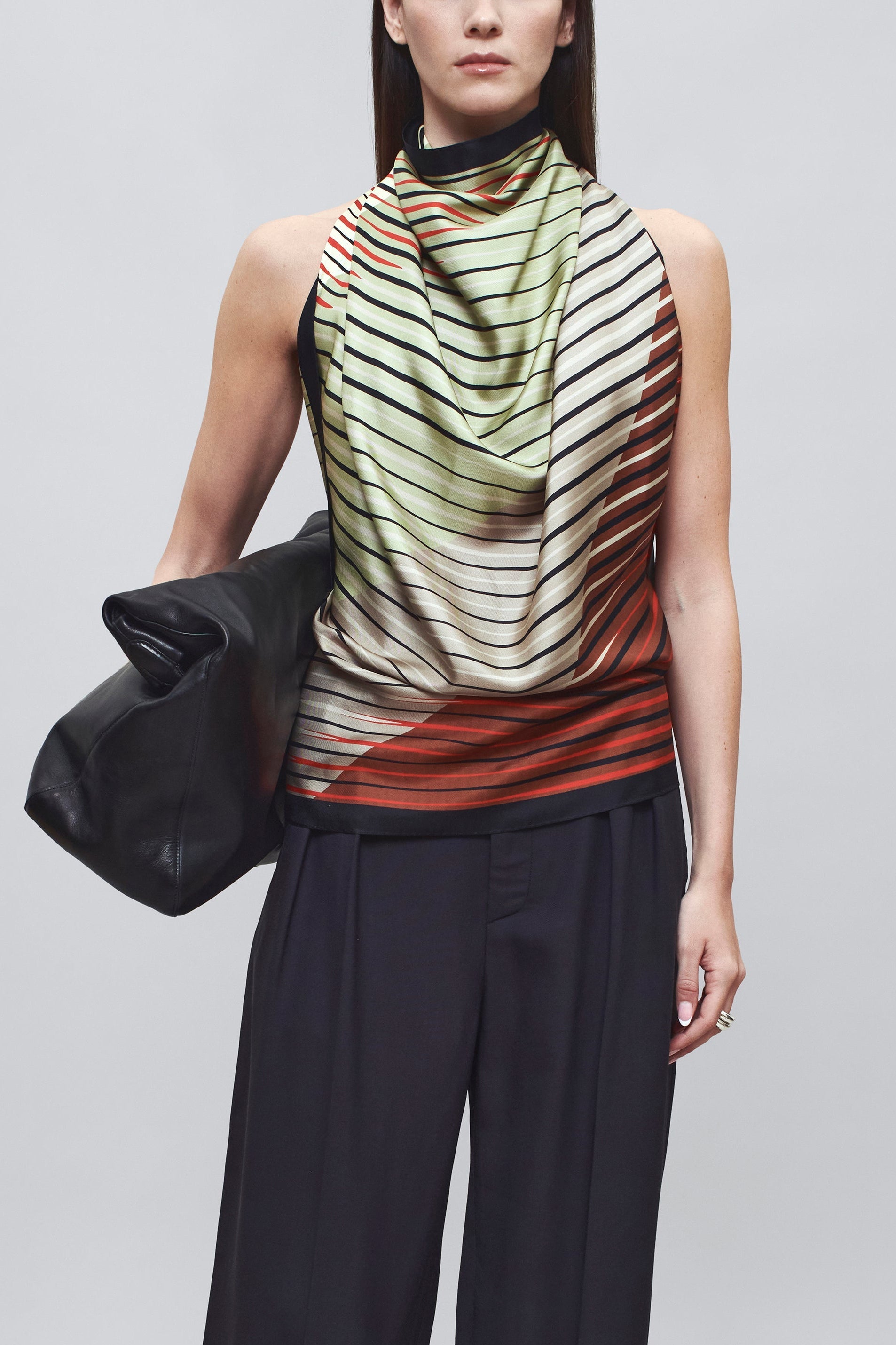 Close-up front view of a woman wearing chic spring summer fashion in a colorful Kallmeyer Neutral Silk Twill Fluted Scarf Top featuring a gradient stripe print, soft cowl neckline, and a deep open back with fitted panel at lower back at an Alas Eius store.
