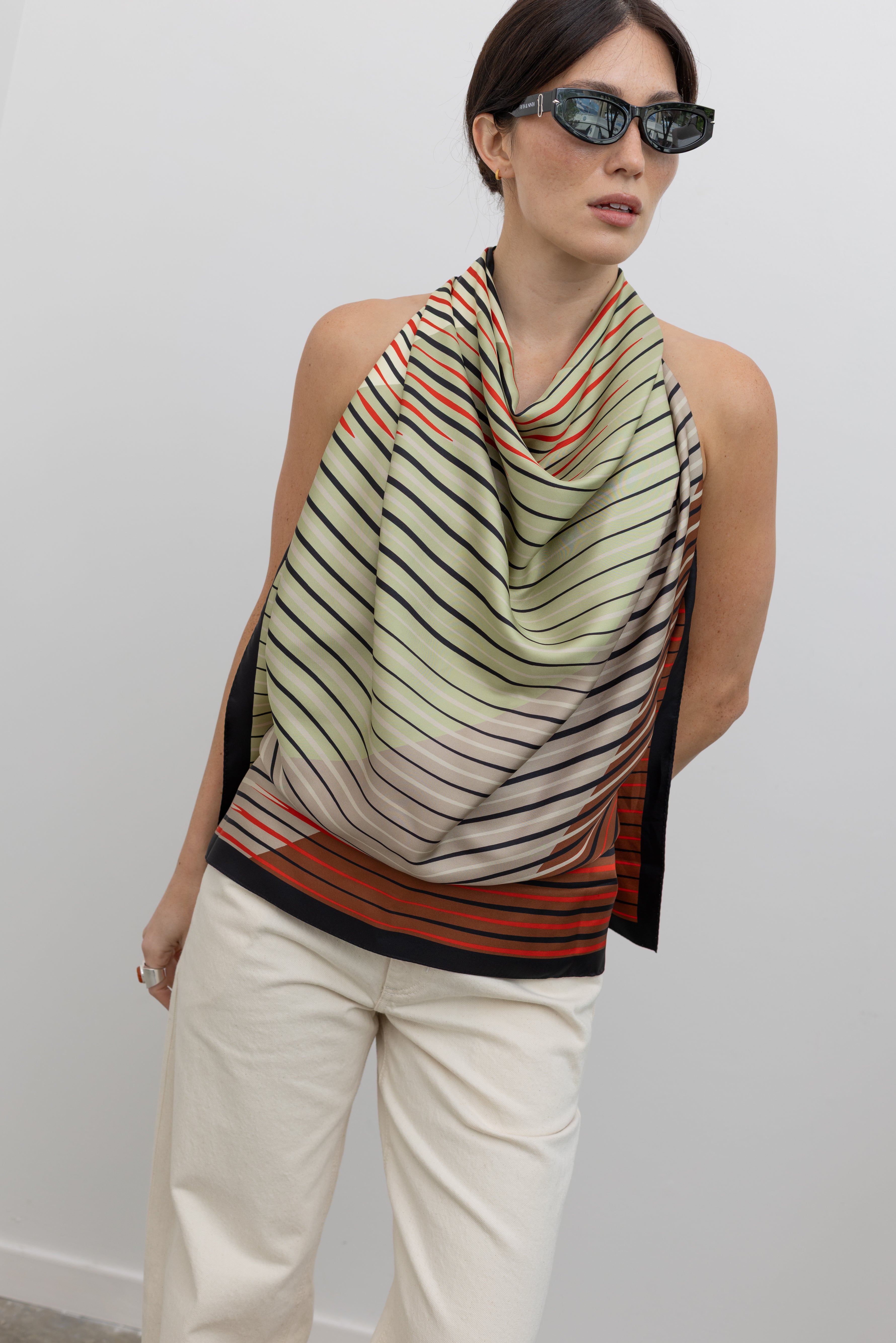 Close-up front view of a woman wearing spring summer fashion in a Kallmeyer Neutral Silk Twill Fluted Scarf Top featuring a gradient stripe print, soft cowl neckline, and a deep open back with fitted panel at lower back and button closure at an Alas Eius store. Made in New York, USA. 