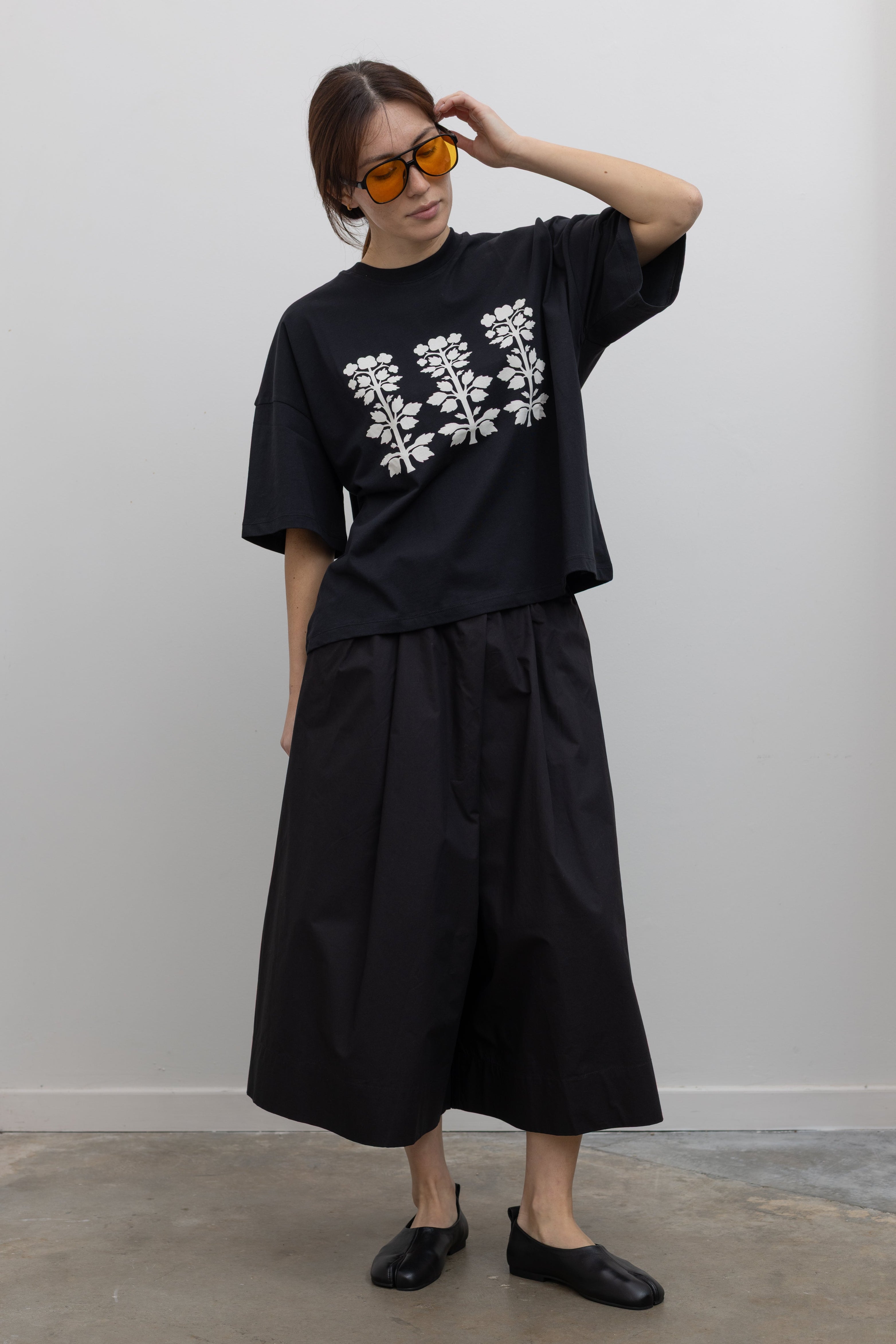 Full front view of a woman standing wearing spring fashion in a Kowtow black cotton jersey relaxed-fit short-sleeve tee featuring a contrasted screen-printed floral design on the front at Alas Eius.