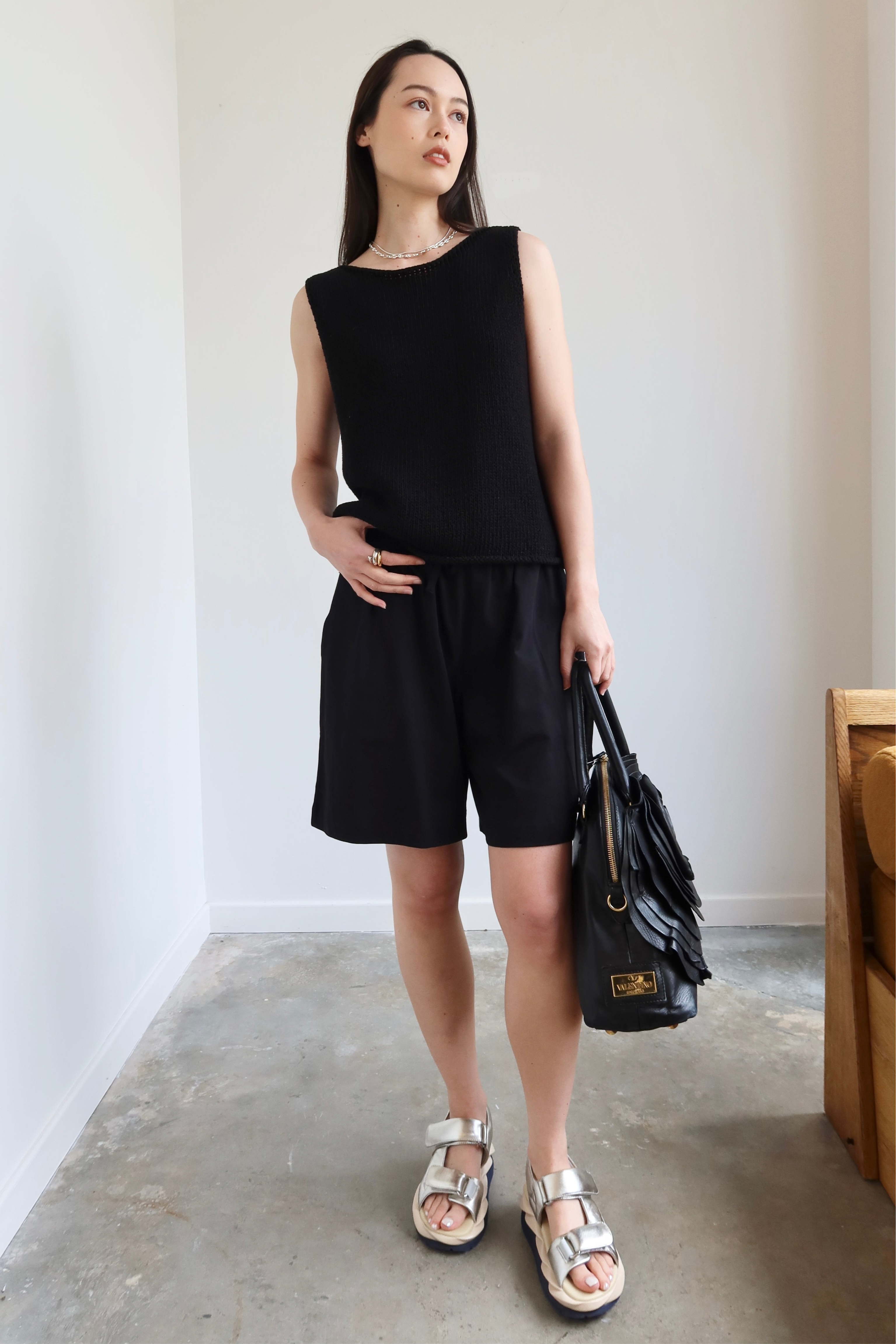 Full front view of a woman standing wearing spring fashion in a sophisticated pair of Kowtow black organic fairtrade cotton drawstring shorts with a black sleeveless top and sandals at Alas Eius. 
