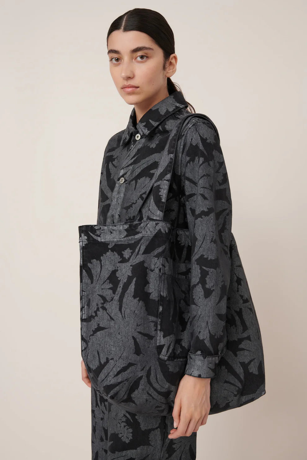 Woman standing with Kowtow etched denim everyday tote bag featuring an oversized pocket on the outside and comfortable wide shoulder straps at Alas Eius.