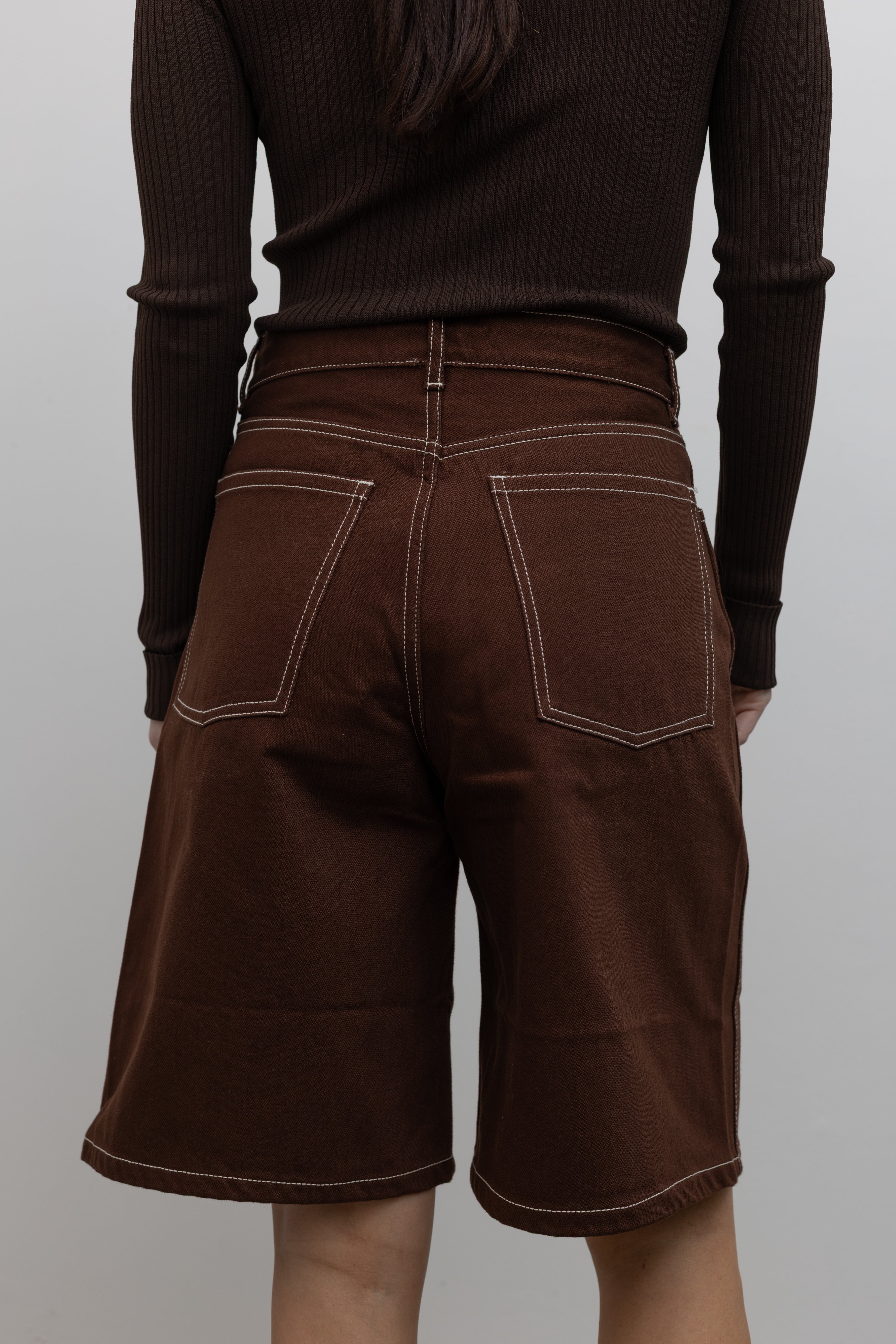 Detailed product view of Woman wearing Spring fashion in a pair of Kowtow Framework Brown relaxed, straight fit Denim Shorts with contrast white topstitching and brown long-sleeved ribbed top at Alas Eius