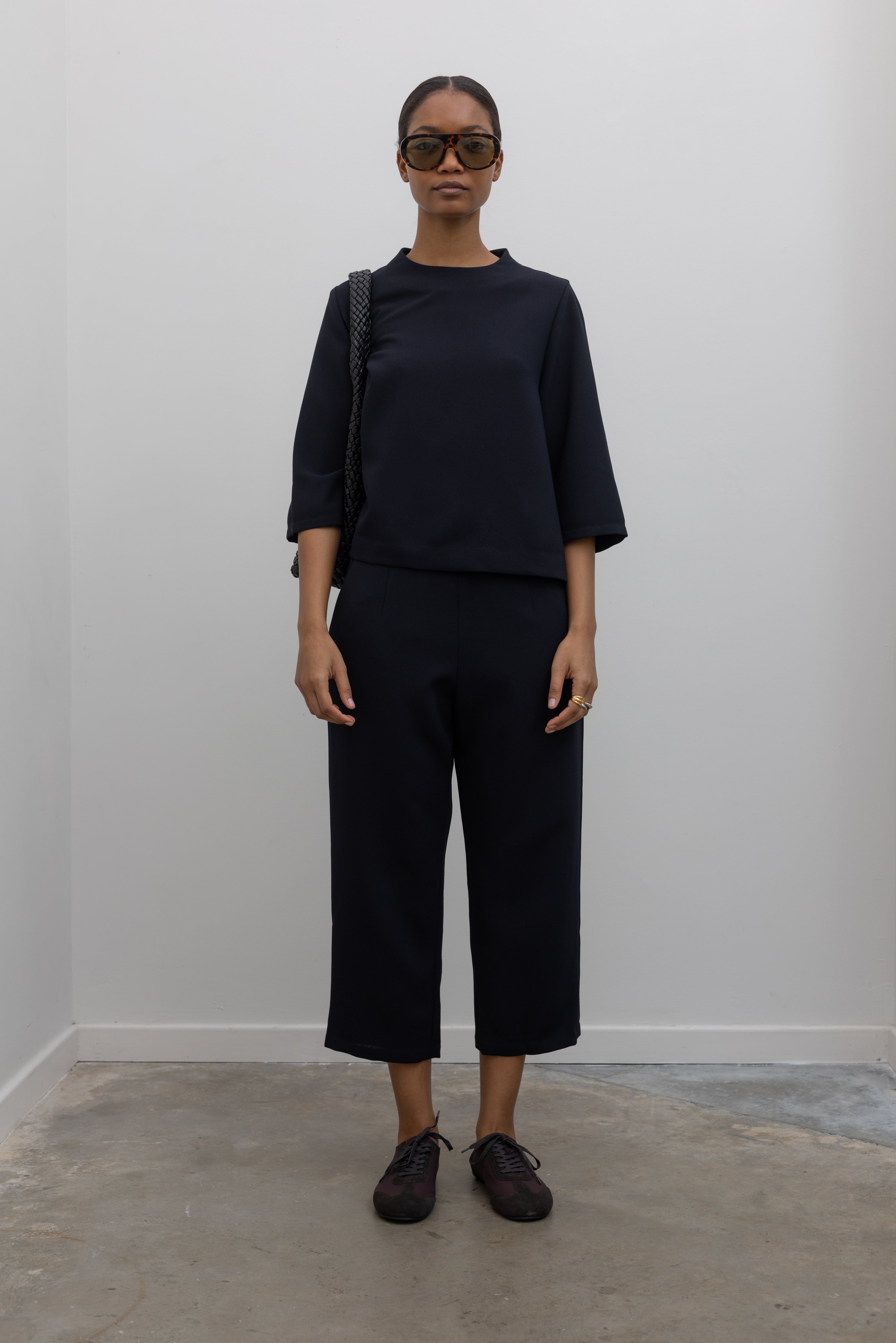 Full length front view of a woman standing wearing the Kaarem Deep Navy Sua Tapered Trouser Pocket Pant with the coordinating top to make the perfect capsule wardrobe set at Alas Eius