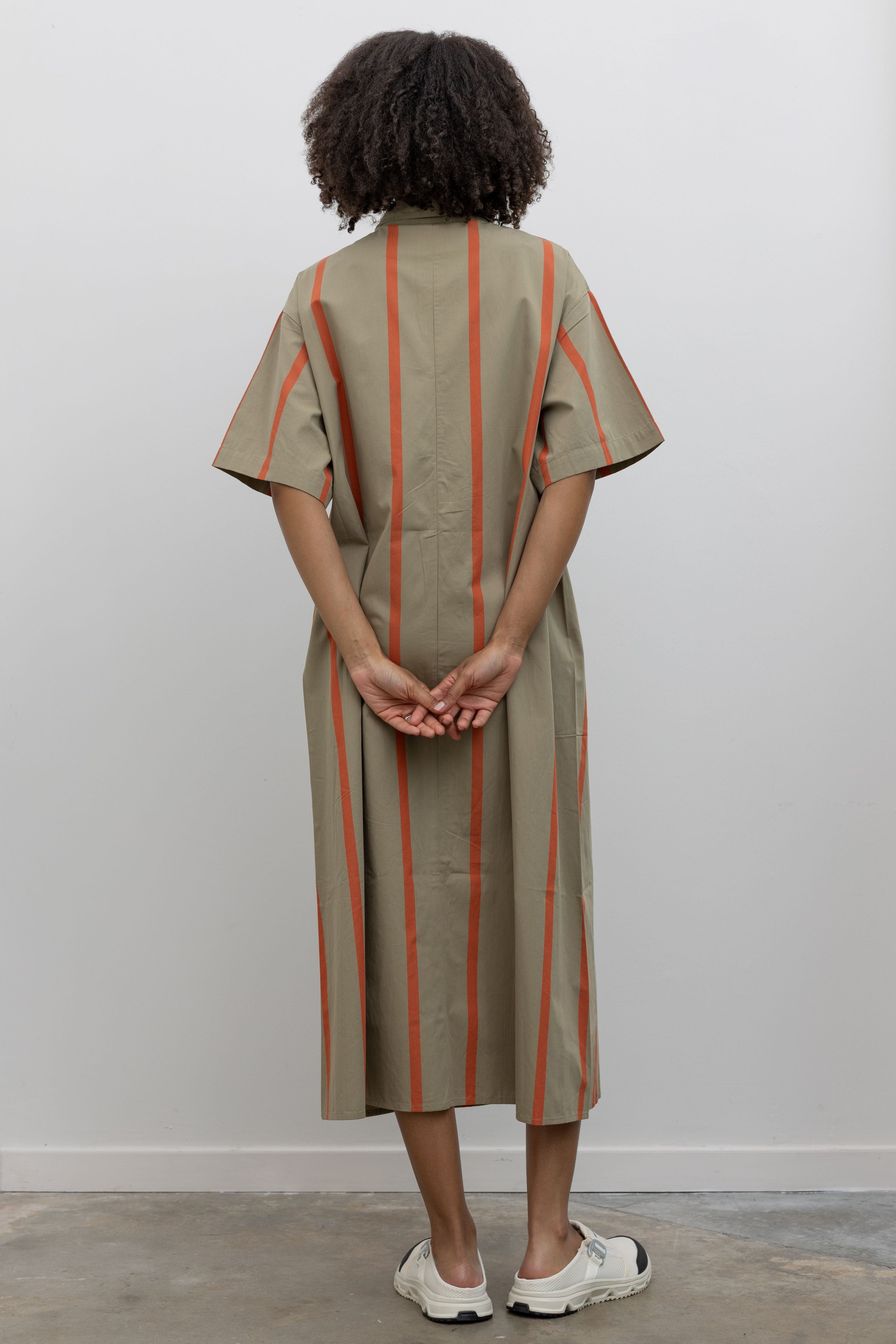 Full length back view of a woman posing wearing an elevated wardrobe staple in a Kowtow Organic Cotton Nasturtium Stripe Oversized Balance Dress featuring pockets, a classic collar, nut buttons down the front at Alas Eius.