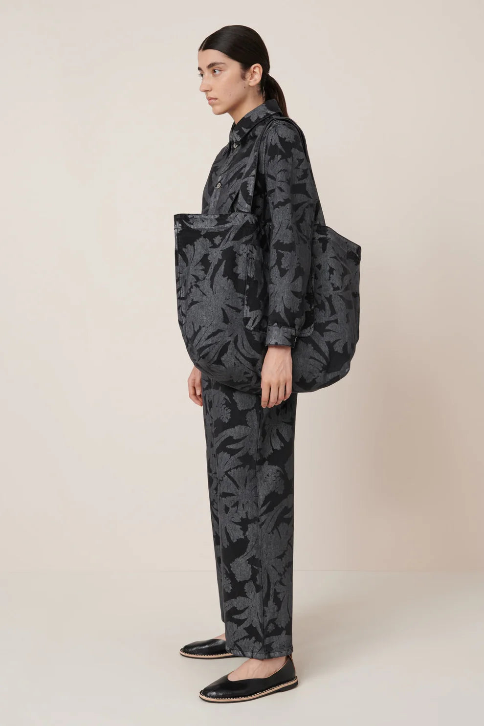 Full view of a woman standing wearing the Kowtow etched denim everyday tote bag featuring an oversized pocket on the outside and comfortable wide shoulder straps at Alas Eius.