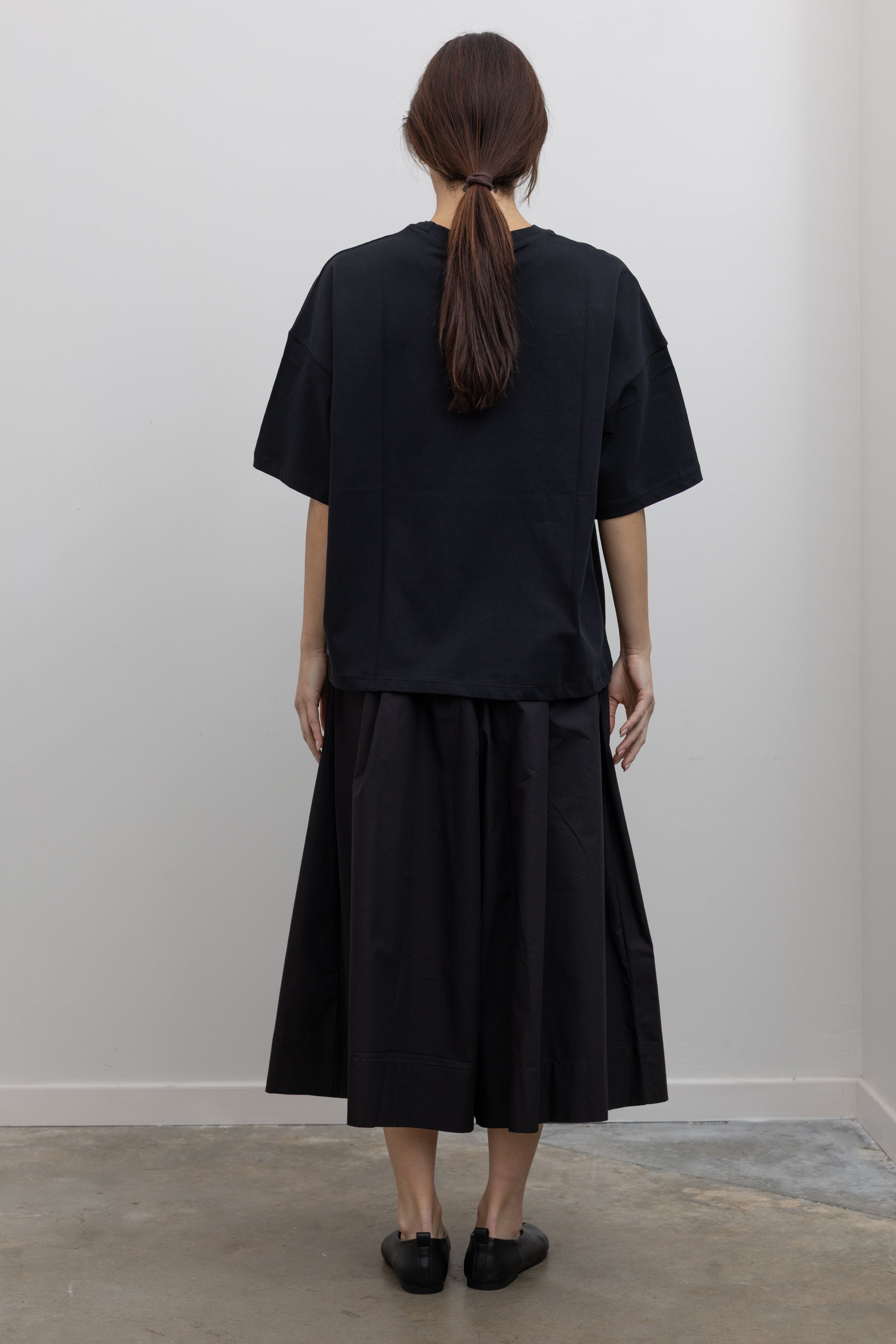 Full back view of a woman standing wearing spring fashion in a Kowtow black cotton jersey relaxed-fit short-sleeve tee featuring a contrasted screen-printed floral design on the front at Alas Eius.