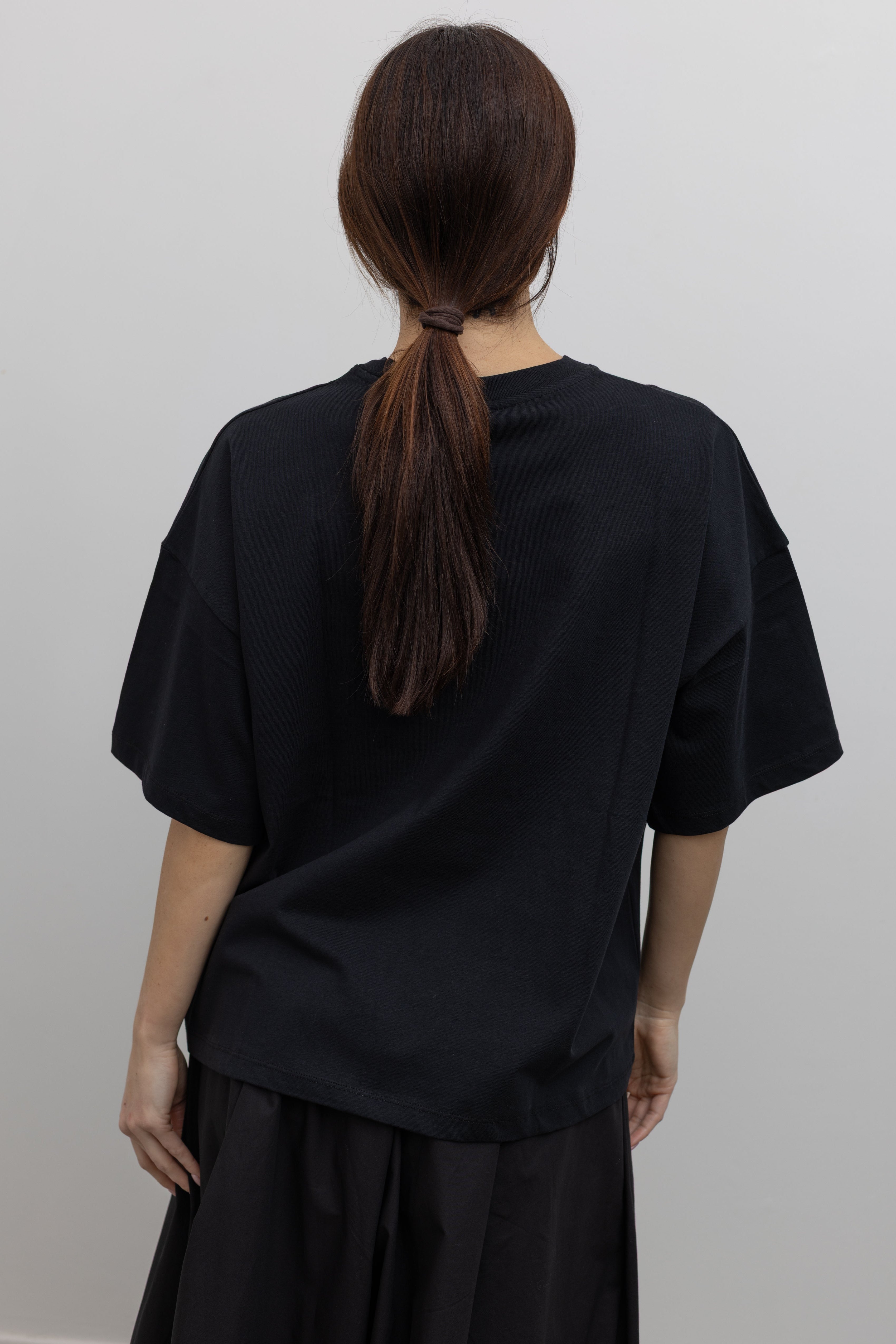 Full back view of a woman standing wearing spring fashion in a Kowtow black cotton jersey relaxed-fit short-sleeve tee featuring a contrasted screen-printed floral design on the front at Alas Eius.