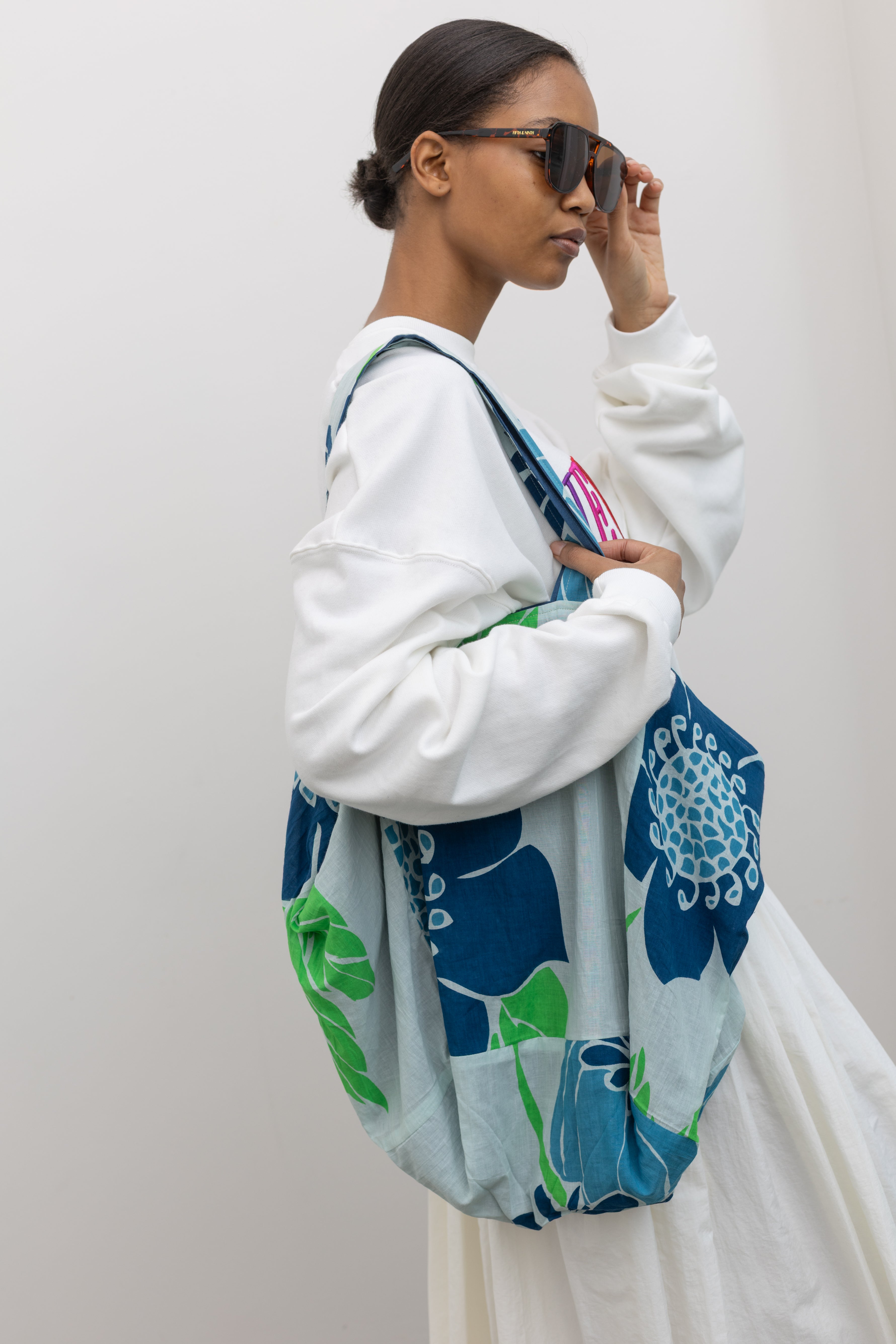 Woman wearing colorful Les Belles Vagabondes brand upcycled organic cotton tote bag with all over vibrant blue and green floral print at Alas Eius. 