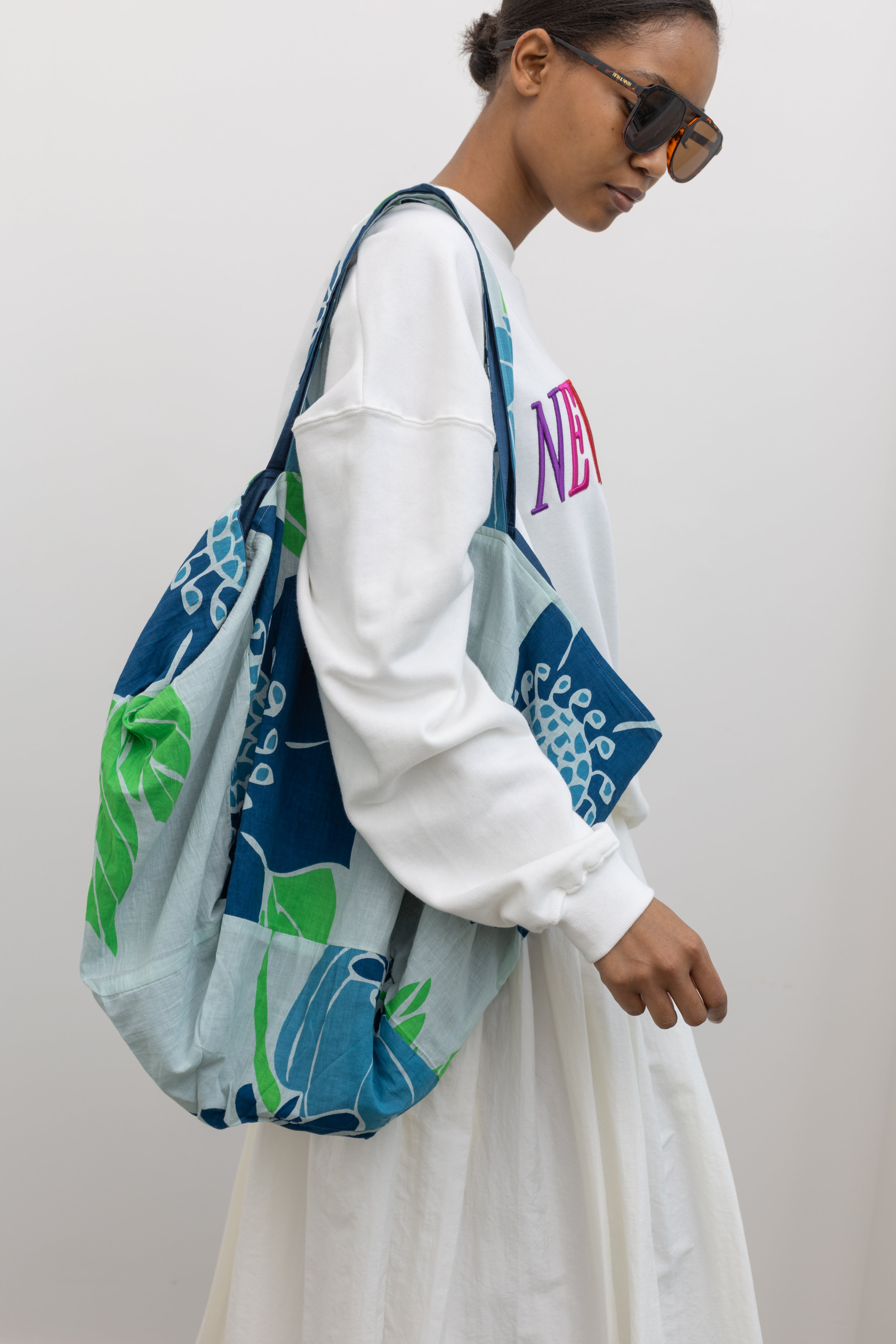 Woman wearing colorful Les Belles Vagabondes brand upcycled organic cotton tote bag with all over vibrant blue and green floral print at Alas Eius. 