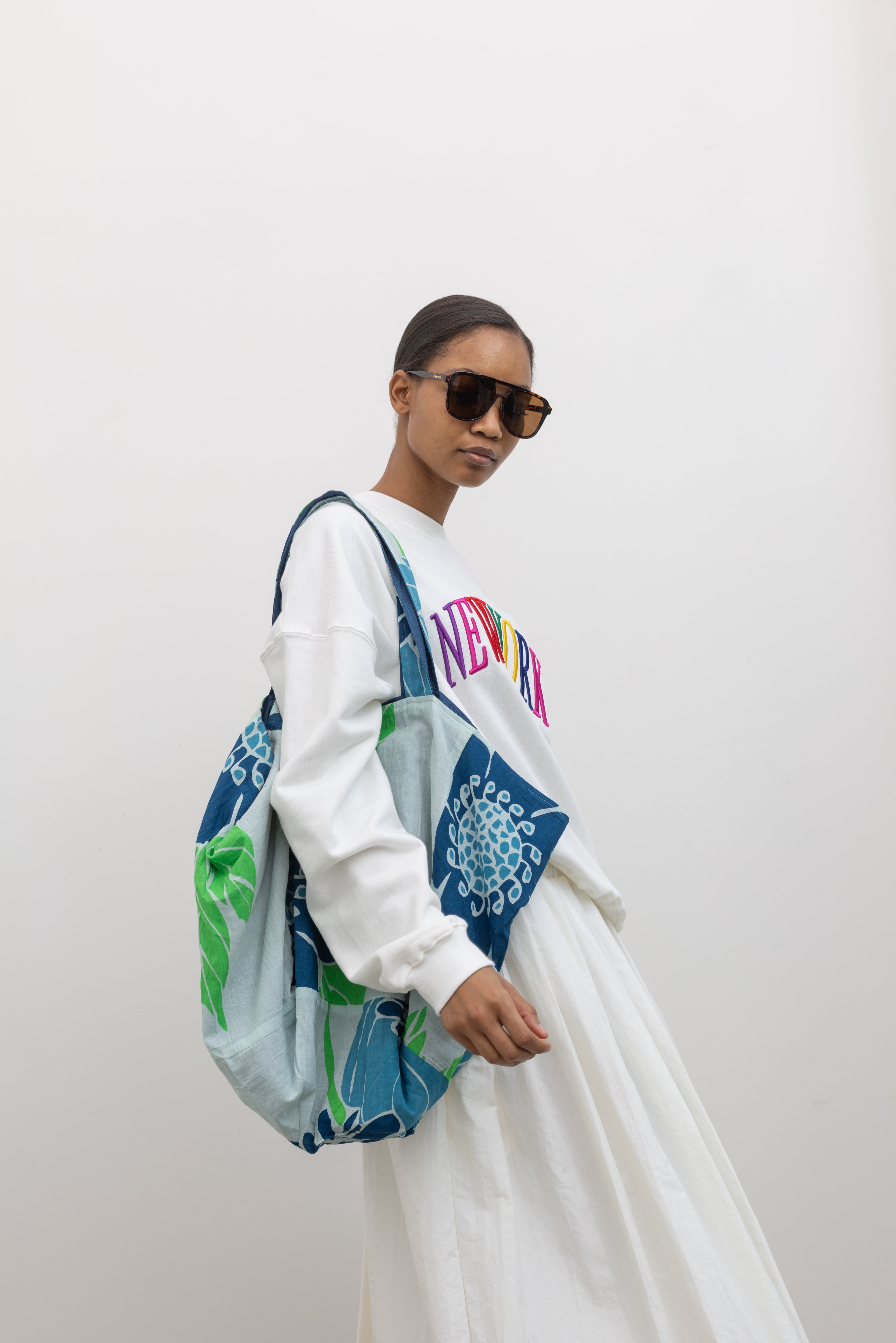 Woman wearing colorful Les Belles Vagabondes brand upcycled organic cotton tote bag with all over vibrant blue and green floral print at Alas Eius. 