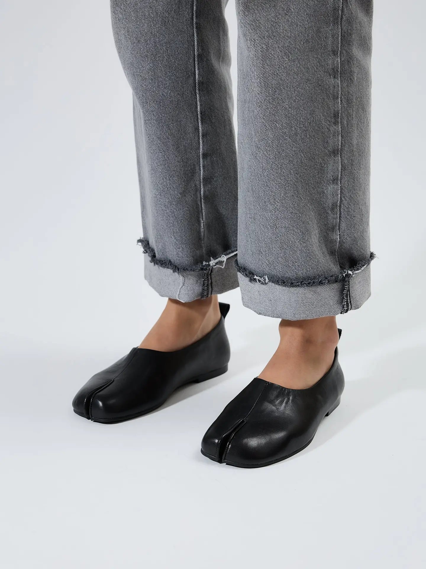 A woman wearing a pair of Lonza NY Black Akaste Leather Tabi Flats with rolled hem denim jeans at Alas Eius