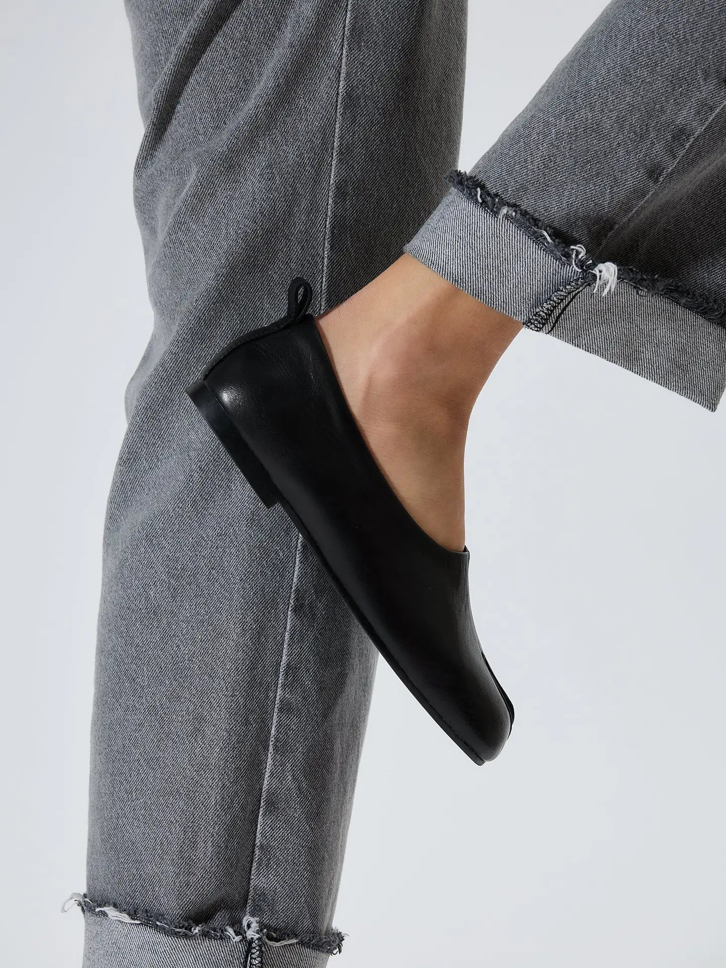 A woman wearing a pair of Lonza NY Black Akaste Leather traditional Japanese inspired Tabi Flats with rolled hem denim jeans at Alas Eius