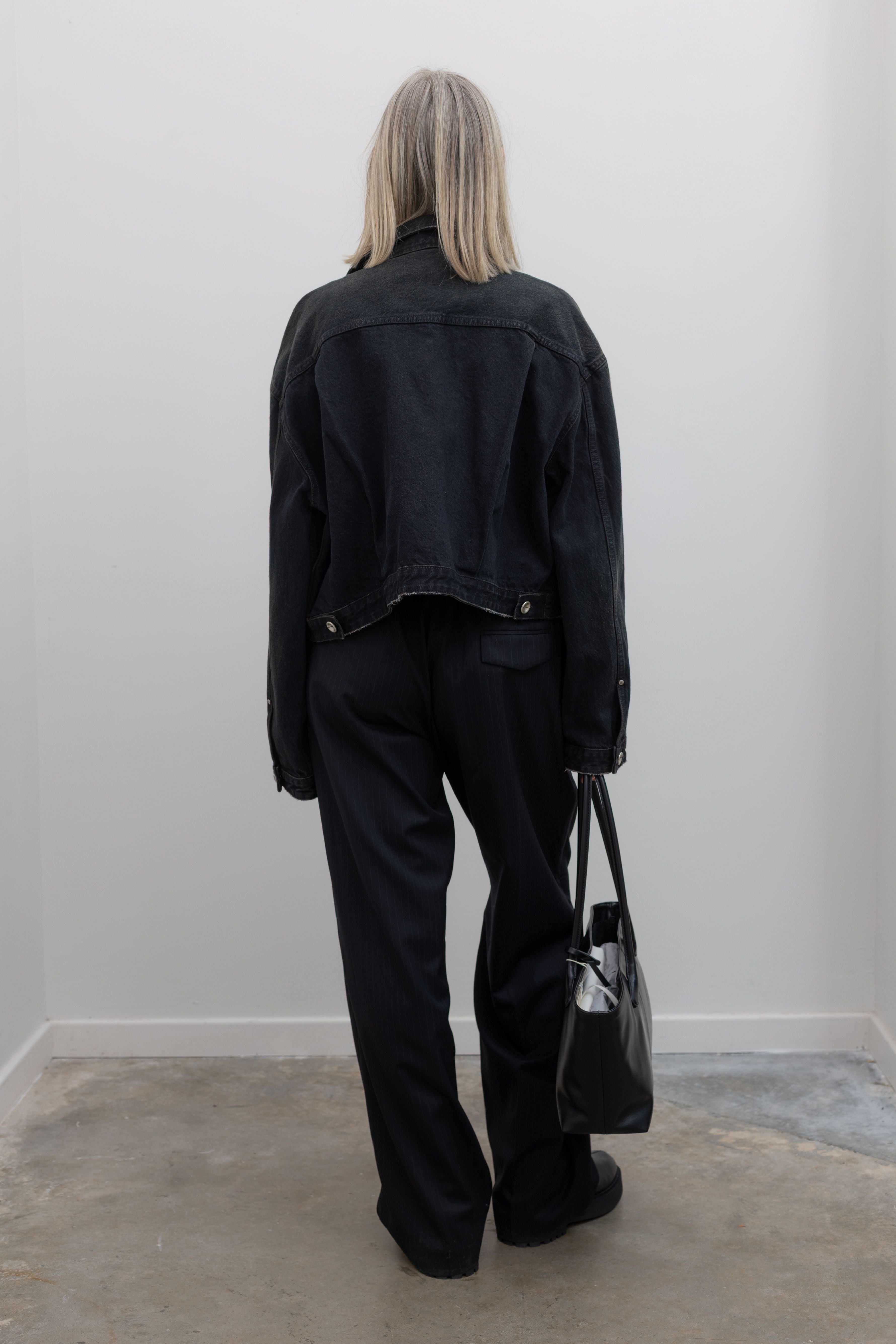 Back view of a woman wearing Low Classic Mahogany Black Denim Short Trucker Jacket featuring silver hardware and a relaxed cropped fit at Alas Eius. 