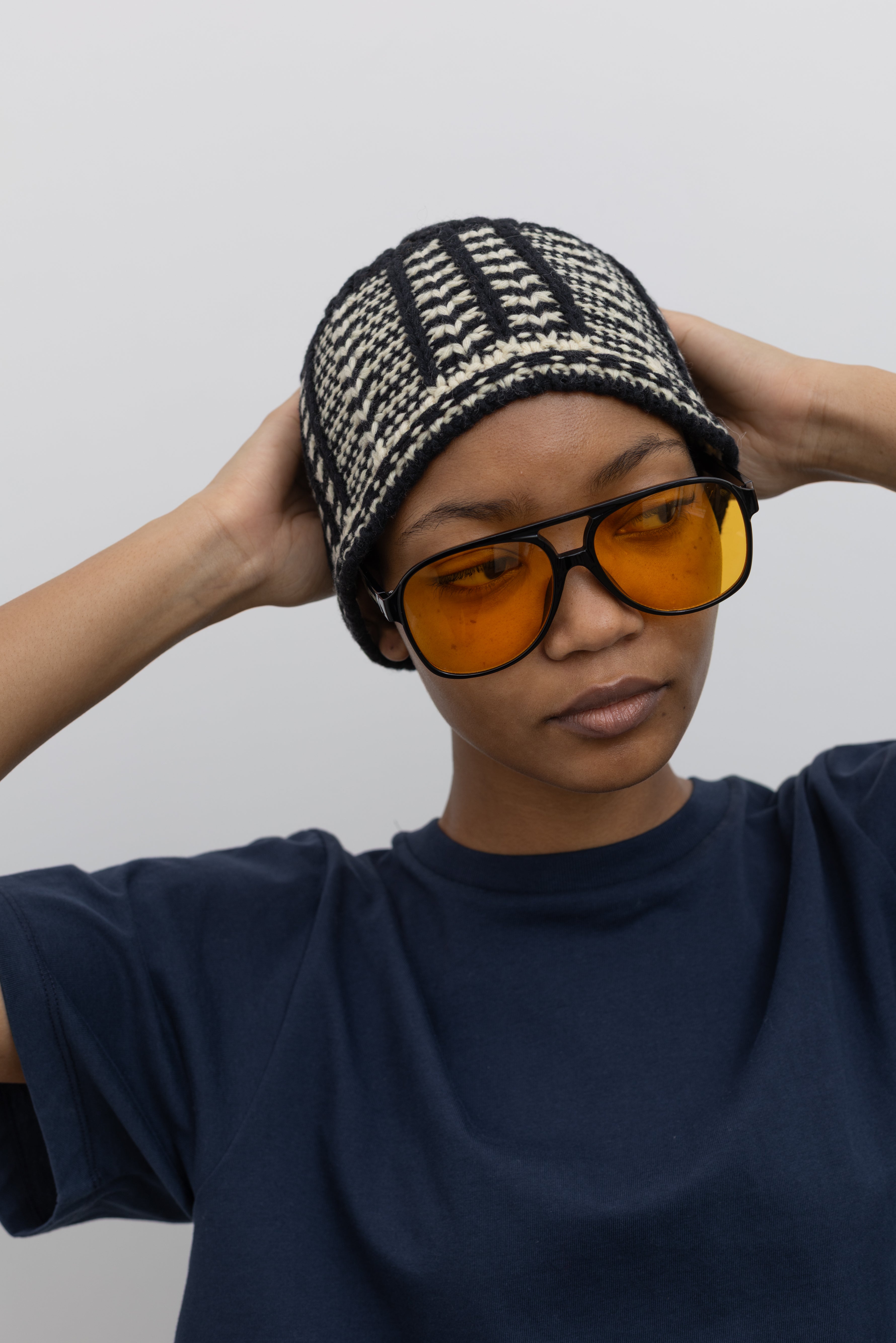 Woman posing with her hands on her head wearing a staple winter fashion accessory in a Low Classic Black And White Jacquard Knit Beanie at Alas Eius. 