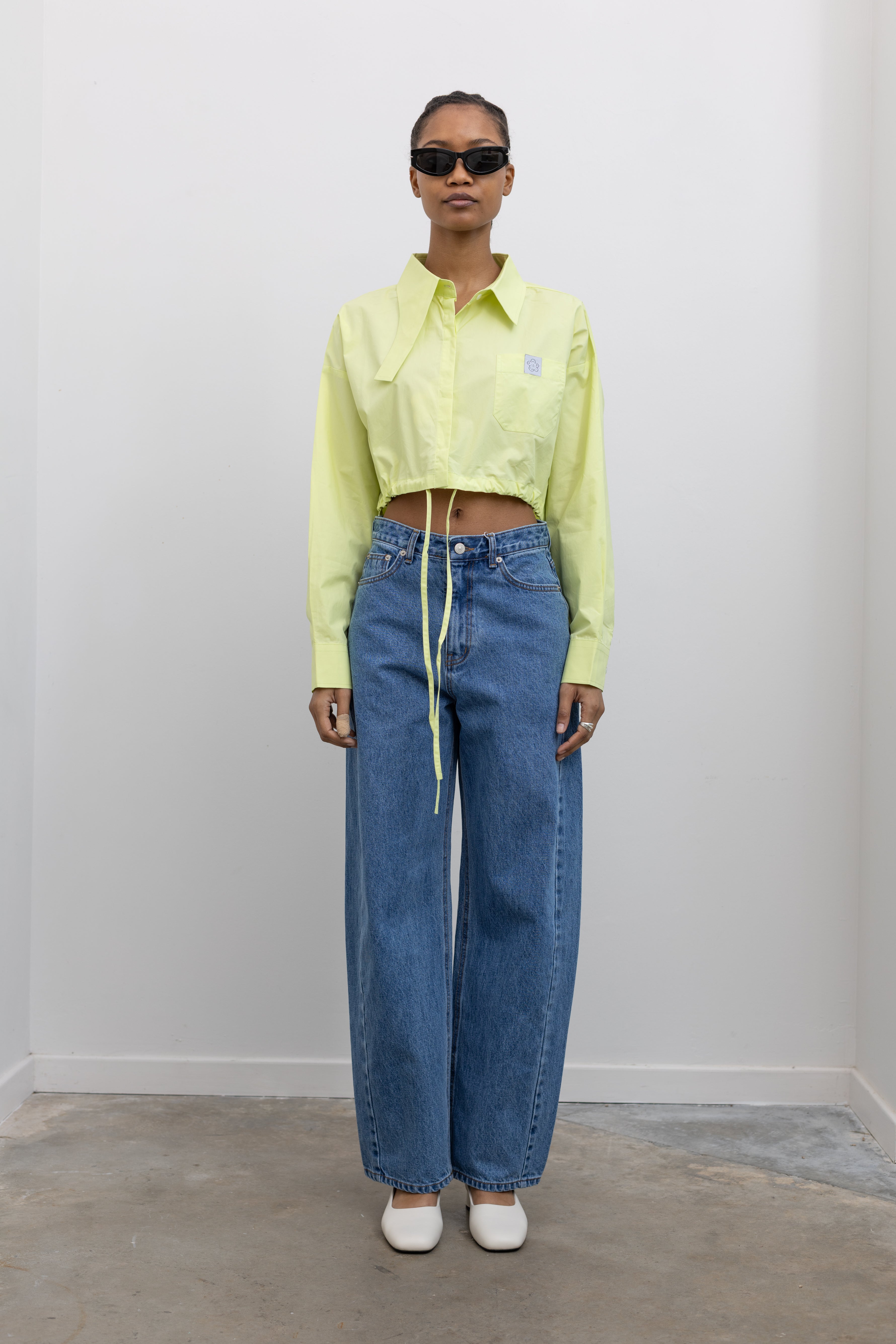 Woman standing wearing Spring fashion in a Mary Lo Citron Long Collar Cropped Button Down Shirt with light wash denim jeans and sunglasses at Alas Eius 