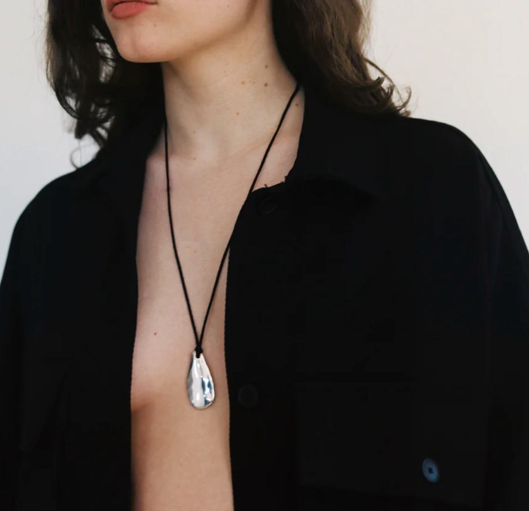 Woman wearing a contemporary style necklace featuring a sterling silver pendant inspired by a tumbled beach stone on a black silk cord at Alas Eius. 