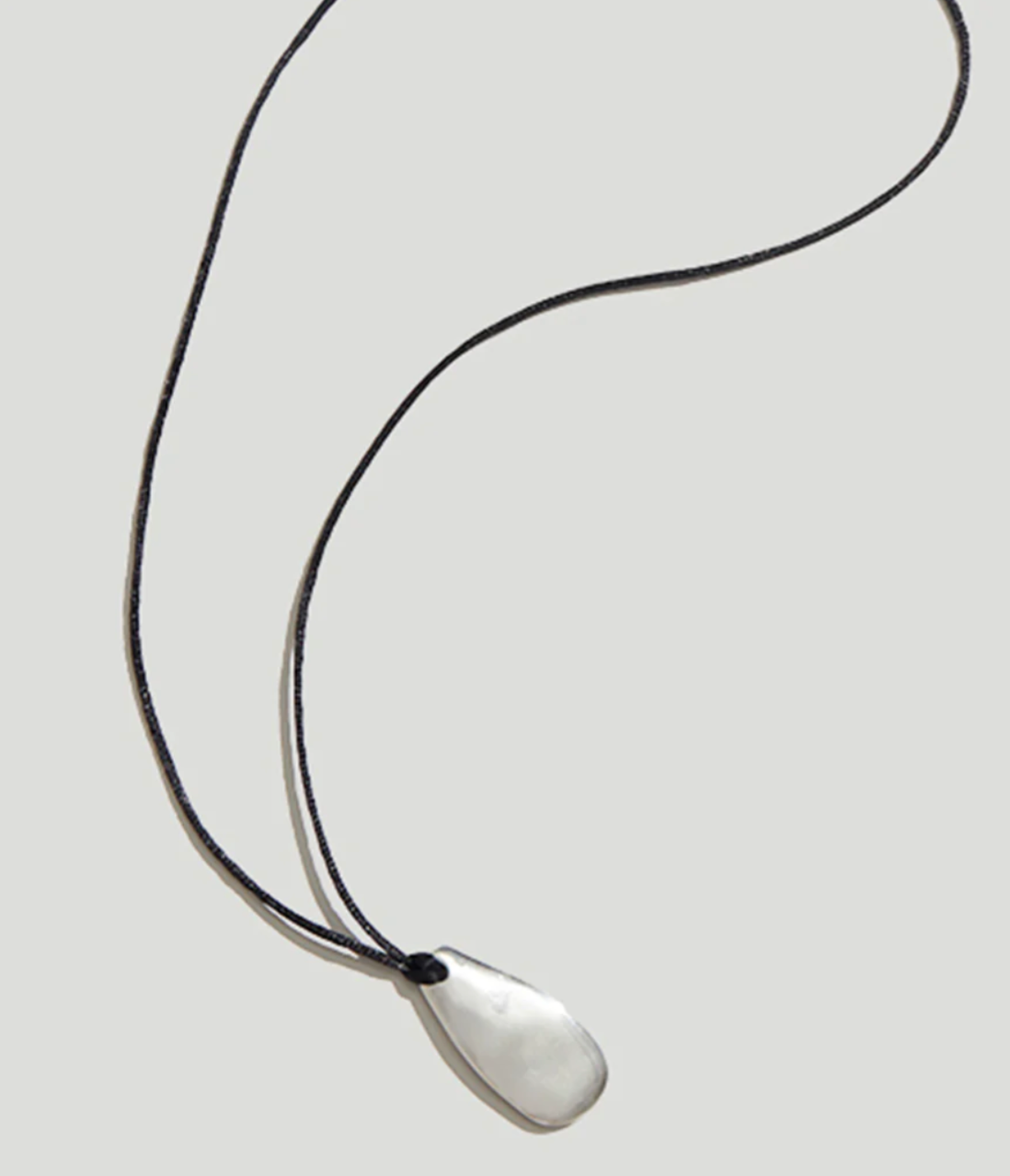 Product view of a contemporary style necklace featuring a sterling silver pendant inspired by a tumbled beach stone on a black silk cord at Alas Eius. 