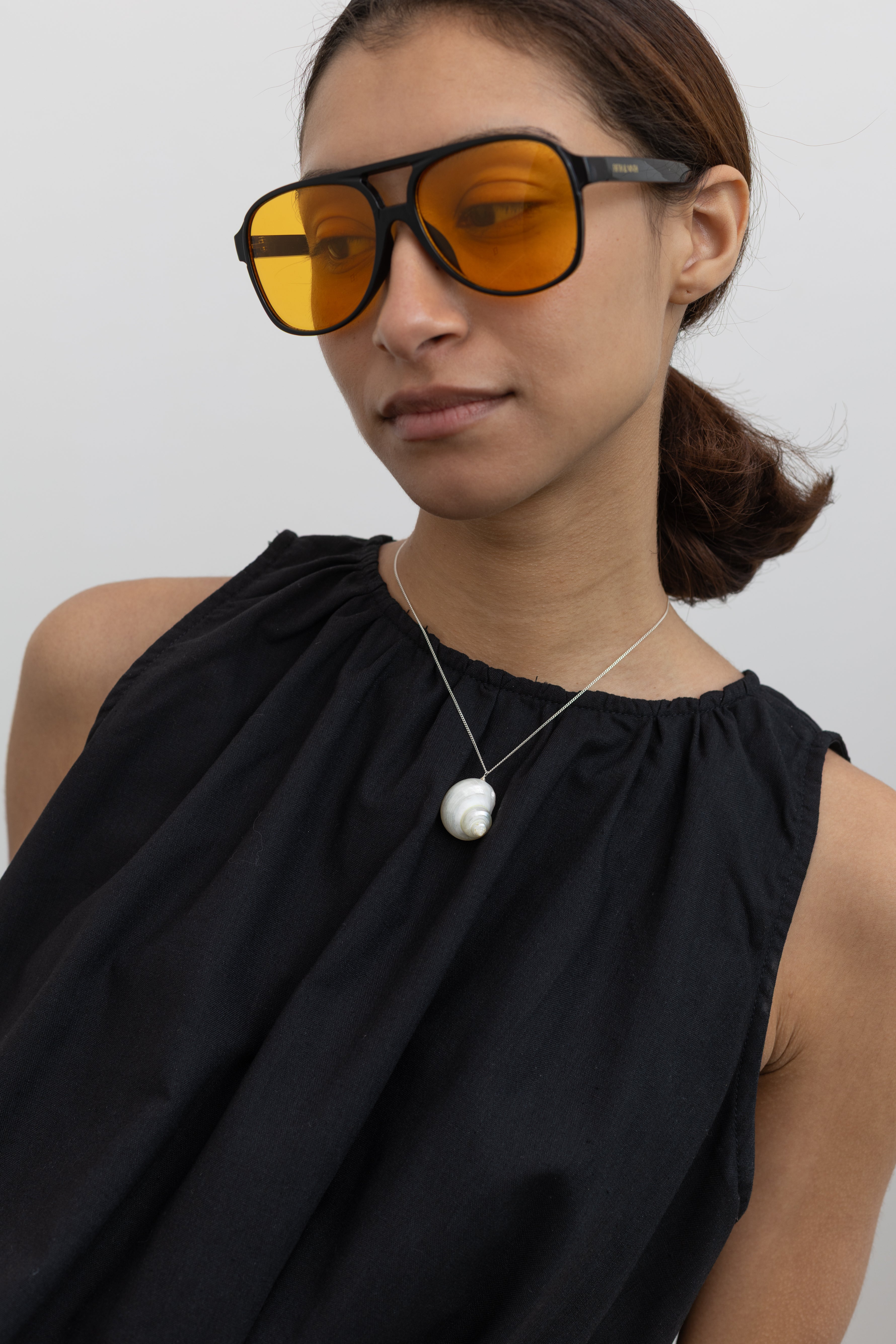 Woman wearing a Maslo necklace featuring a white shell charm pendant on a fine sterling silver chain paired with a black gathered neckline top at Alas Eius. 