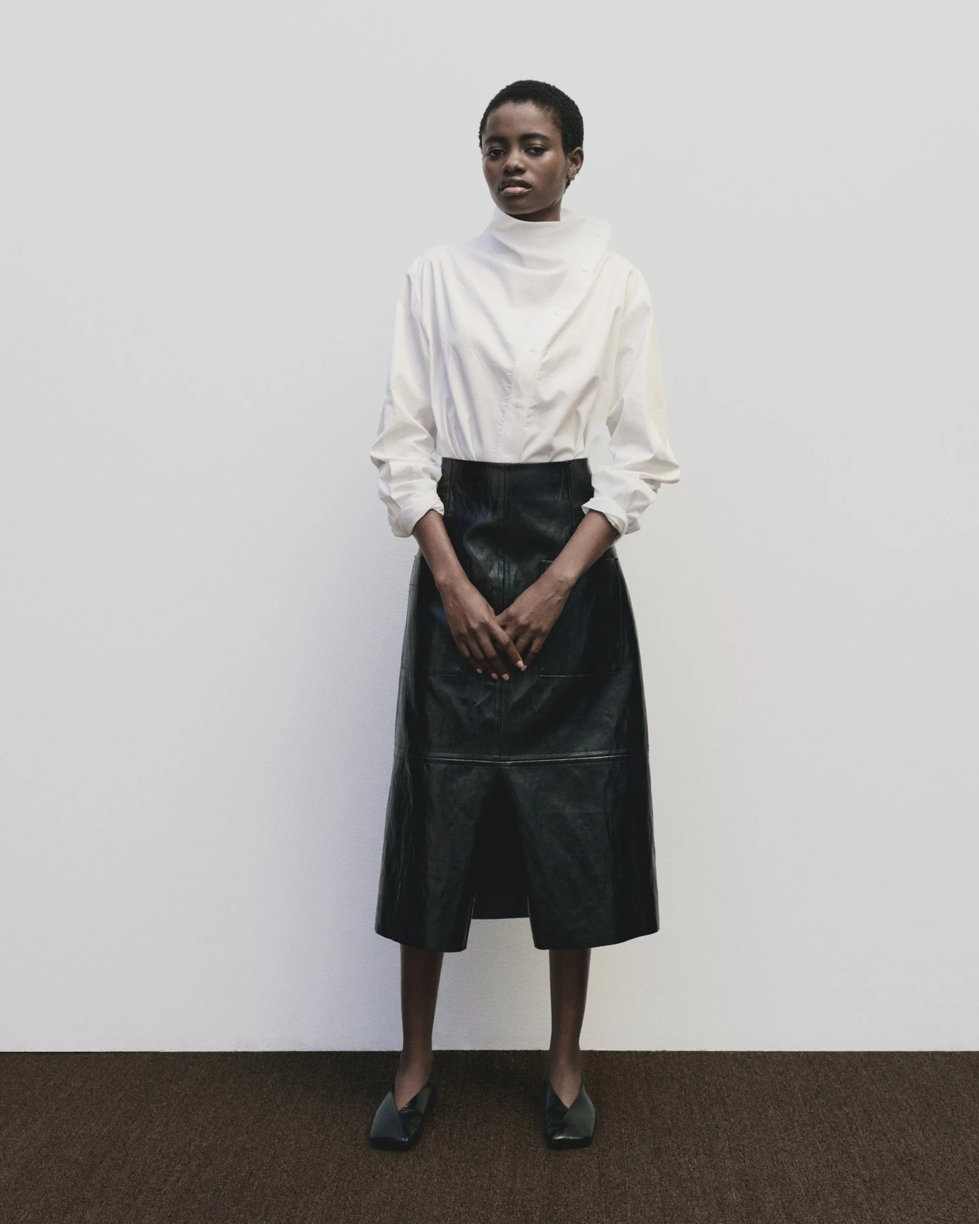 Person wearing a white blouse and black leather skirt against a plain background