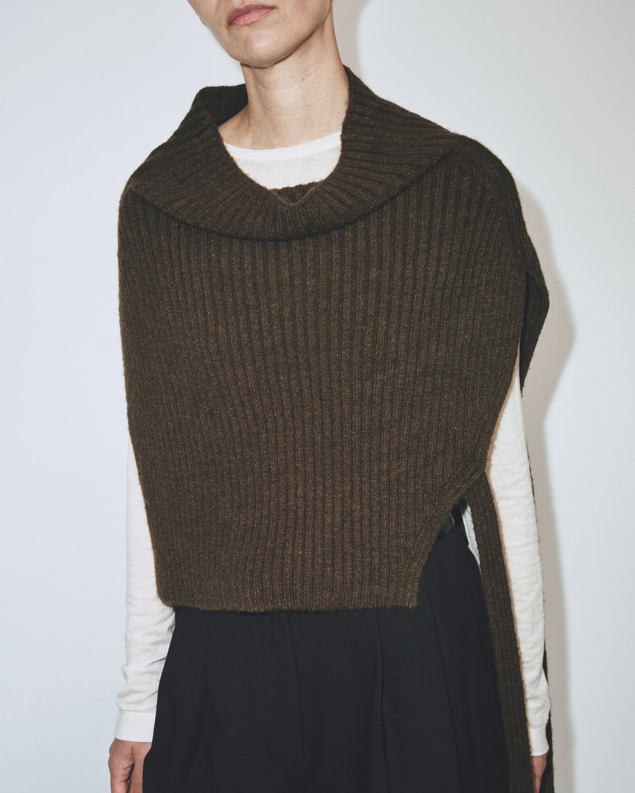 A person wearing an olive brown ribbed knitted Mijeong Park neck warmer with a mock neck neckline and tie waist detail, paired with black pants at Alas Eius