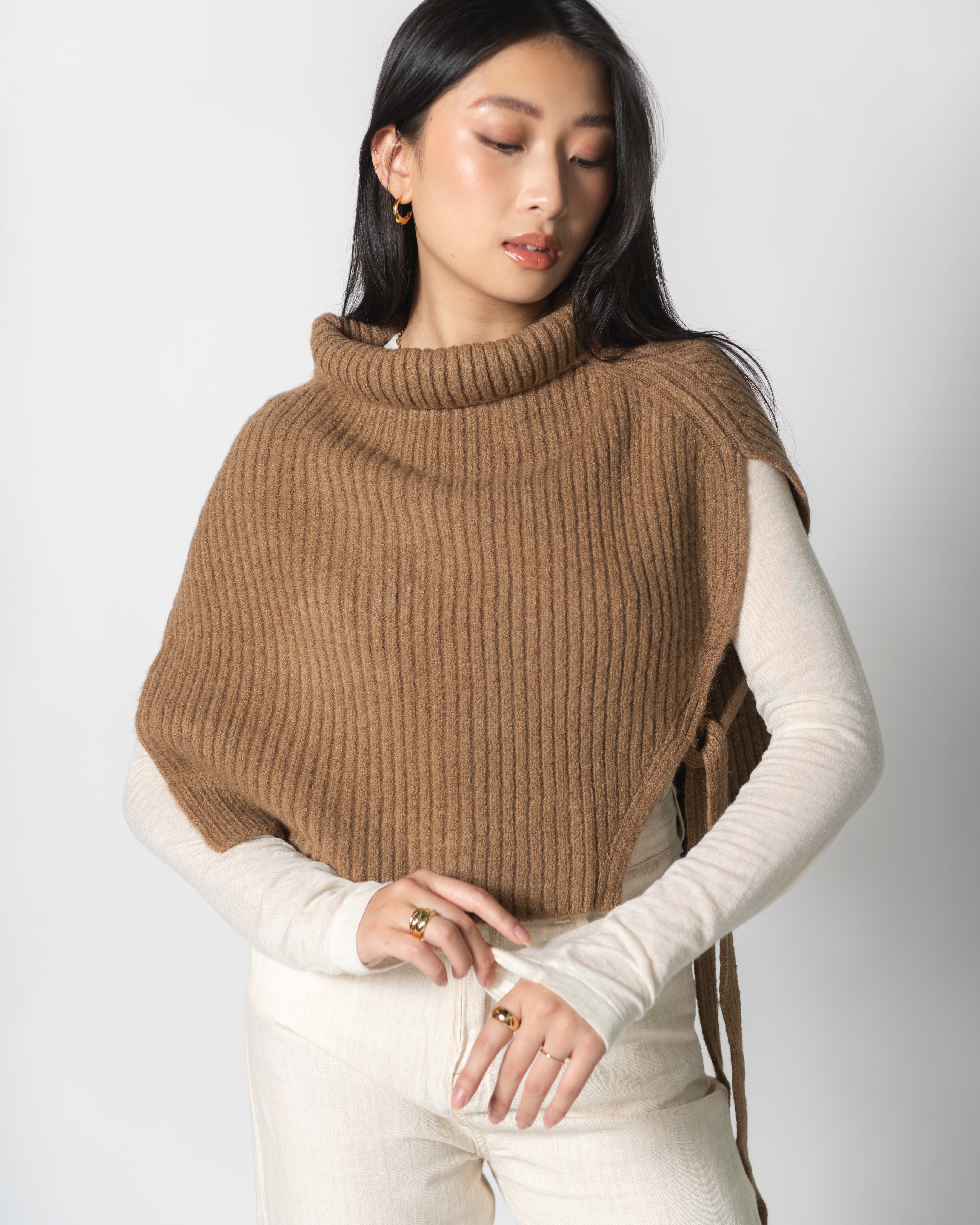 A woman wearing a brown ribbed neck warmer over a white top, paired with beige pants.