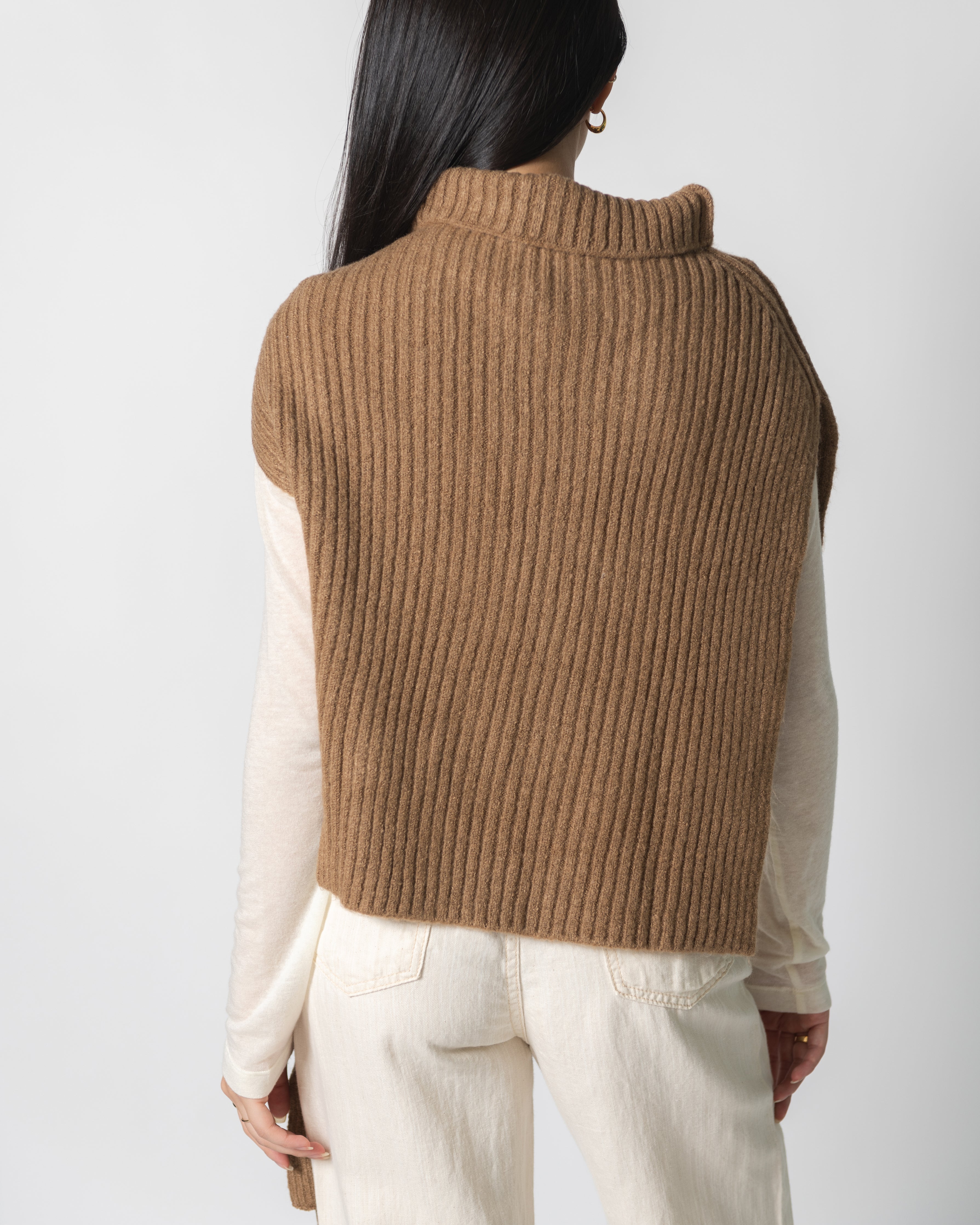 A woman wearing a brown ribbed neck warmer over a white top, paired with beige pants.