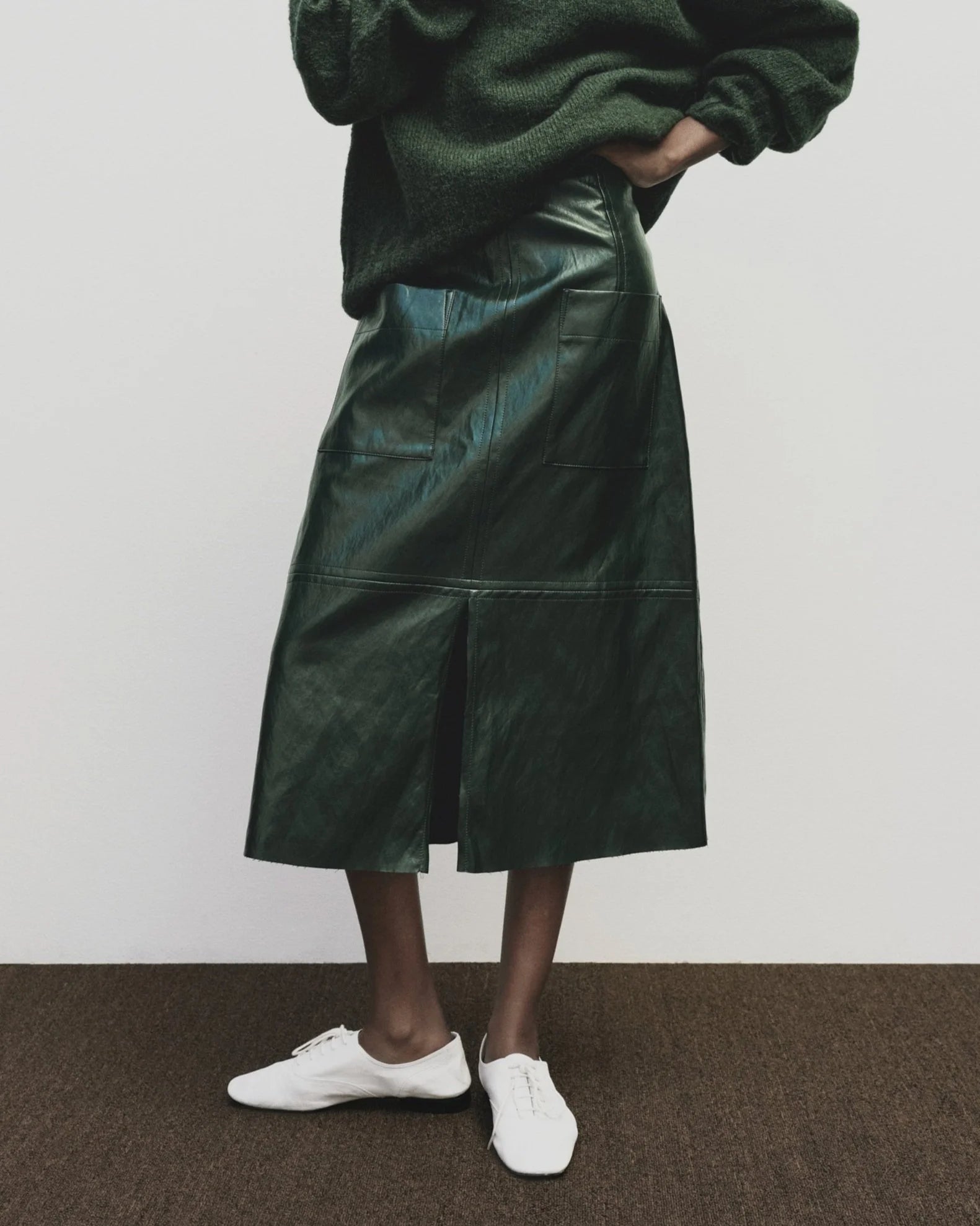 Person wearing a green leather skirt and white shoes on a plain background