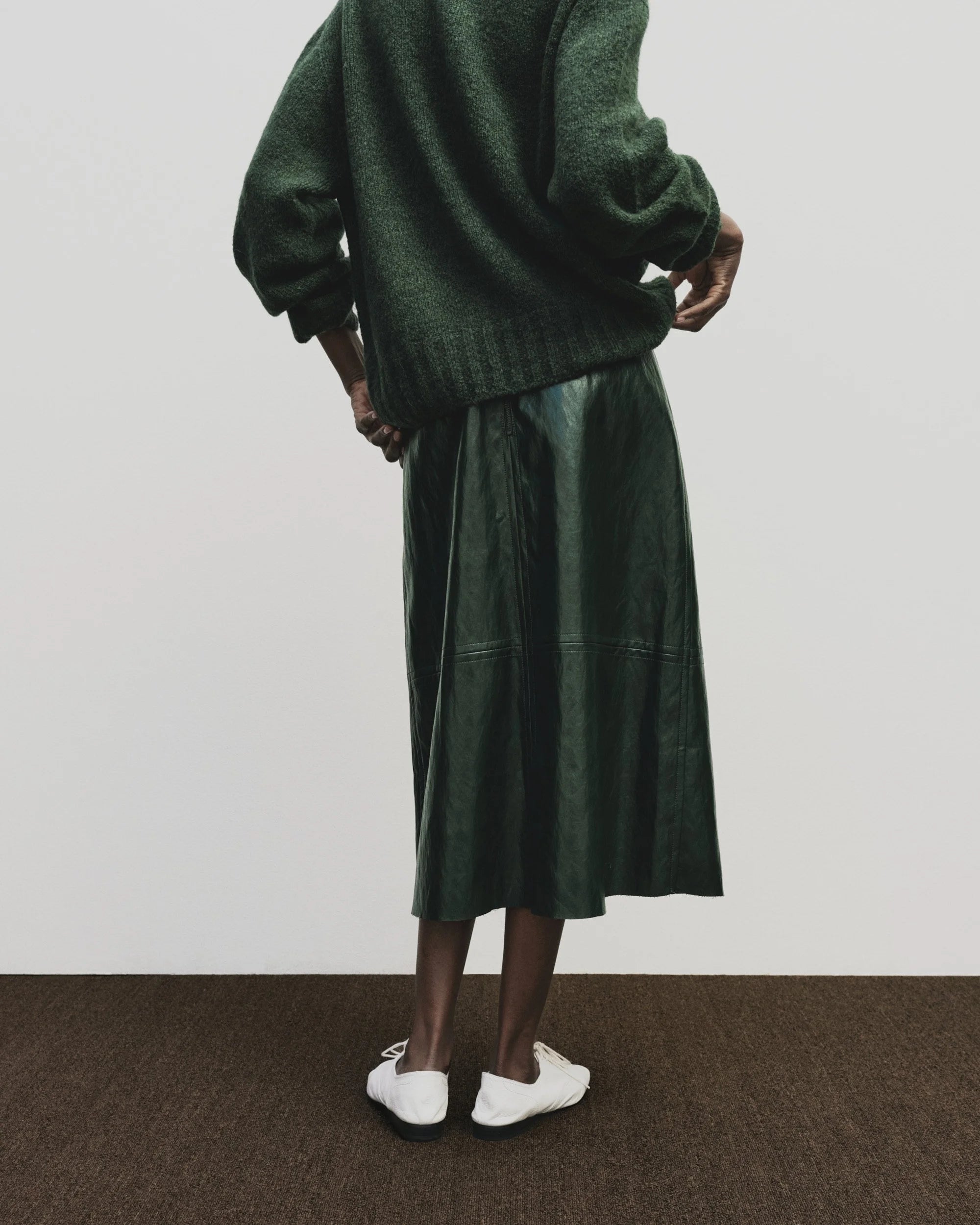 Person wearing a green sweater and skirt with white shoes on a plain background