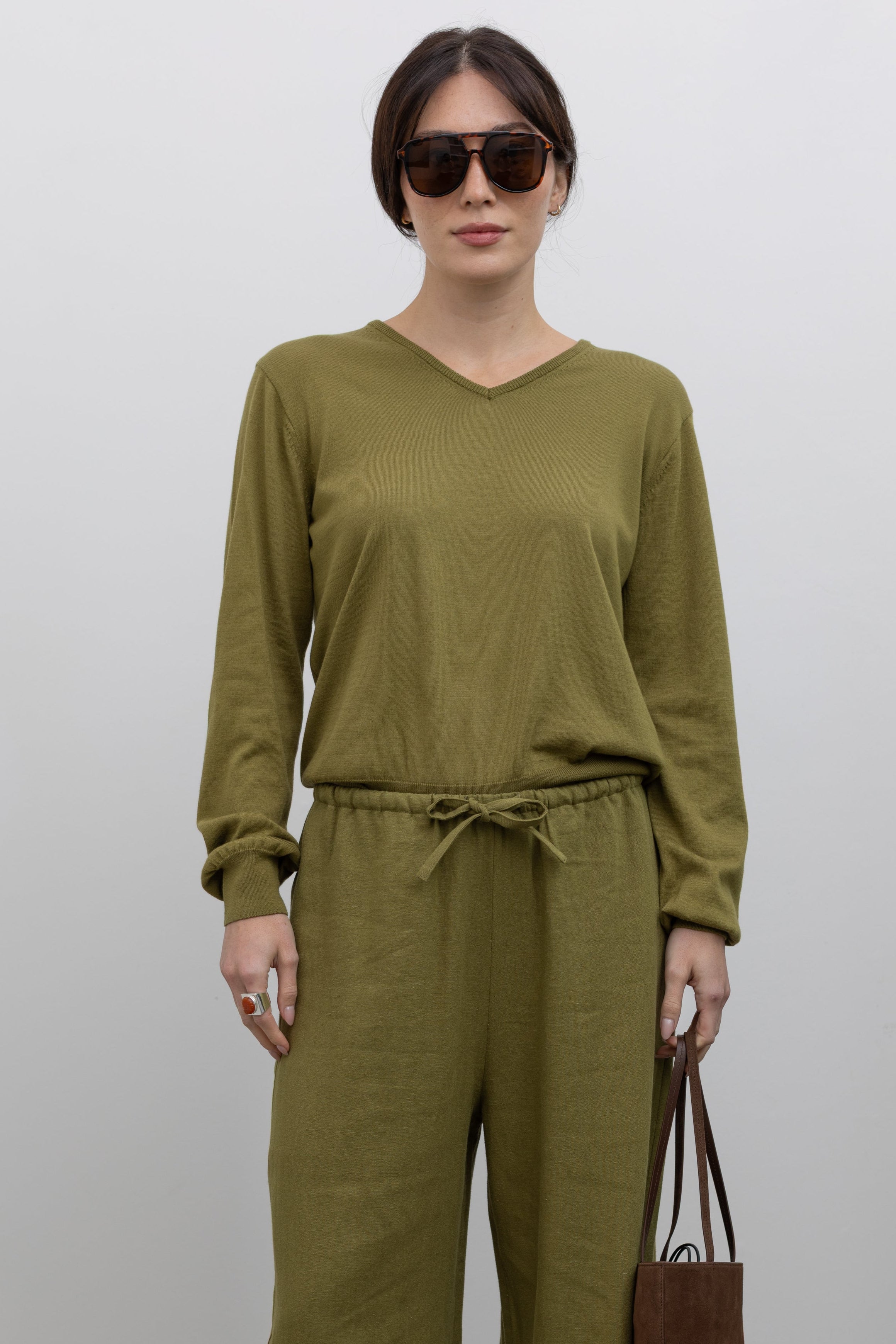 Full length front view of a woman posing wearing elevated casual spring fashion in the Mijeong Park Soft Green Cotton Blend V-Neck Knit Long Sleeve Top paired with Mijeong Park Green Linen Blend Wide Leg Cropped Pants featuring a comfortable drawstring waist, front and back patch pockets, and a cropped length suitable for a minimalist, versatile wardrobe at an Alas Eius store. 