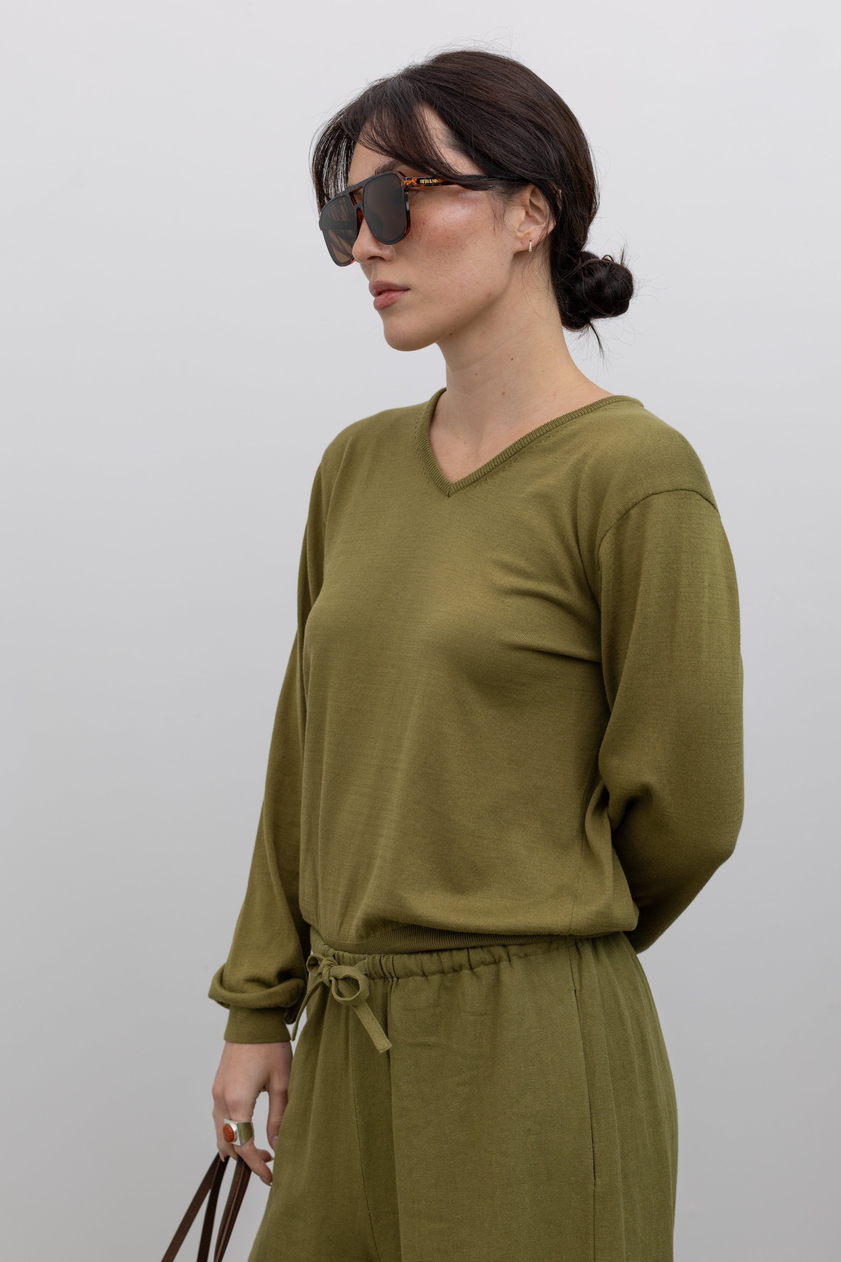 Close-up 3/4 view of a woman posing wearing elevated casual spring fashion in the Mijeong Park Soft Green Cotton Blend V-Neck Knit Long Sleeve Top paired with Mijeong Park Green Linen Blend Wide Leg Cropped Pants featuring a comfortable drawstring waist, front and back patch pockets, and a cropped length suitable for a minimalist, versatile wardrobe at an Alas Eius store. 