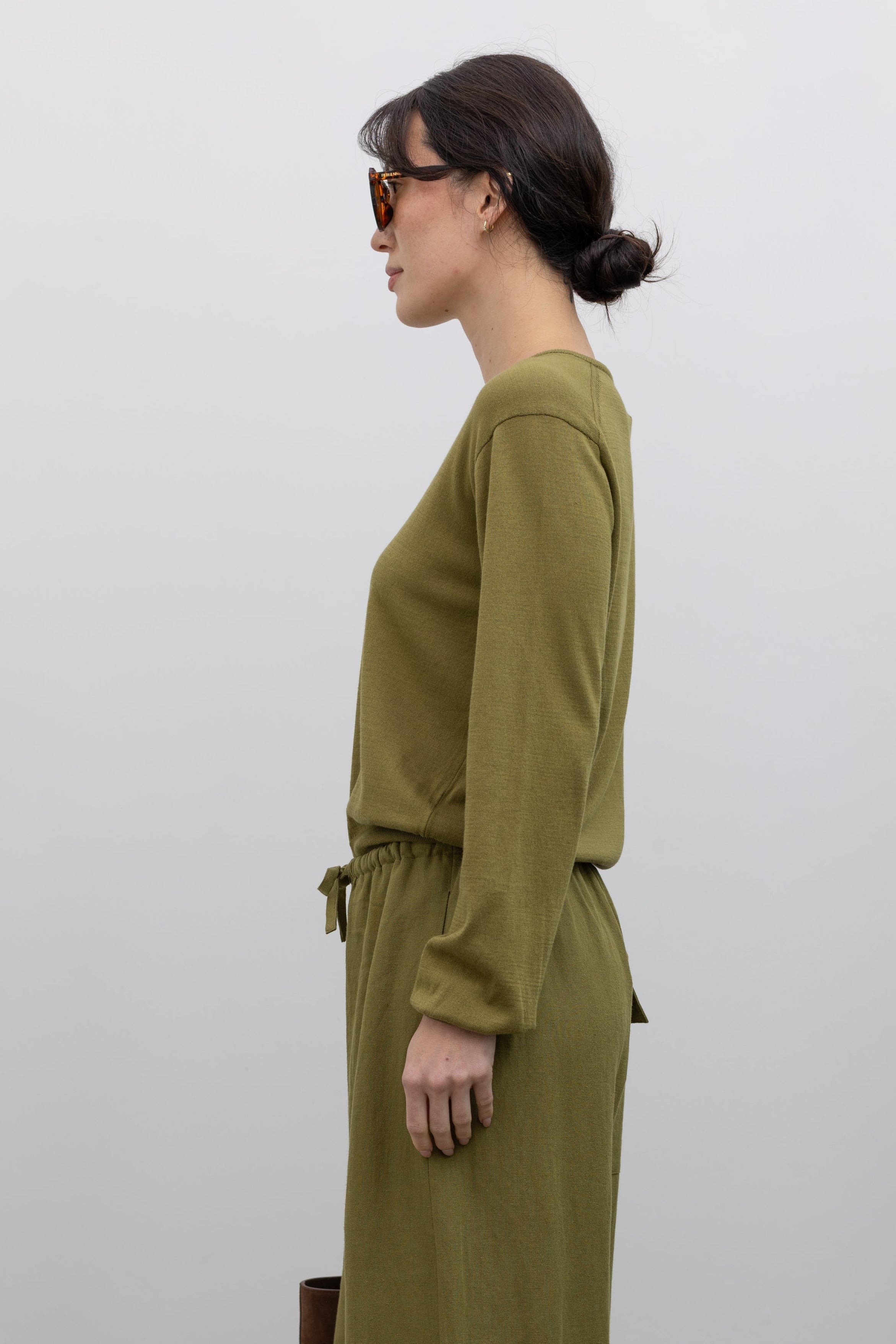 Full length front view of a woman posing wearing elevated capsule wardrobe essentials in the Mijeong Park Soft Green Cotton Blend V-Neck Knit Long Sleeve Top paired with Mijeong Park Green Linen Blend Wide Leg Cropped Pants featuring a comfortable drawstring waist, front and back patch pockets, and a cropped length suitable for a minimalist, versatile wardrobe at an Alas Eius store. 
