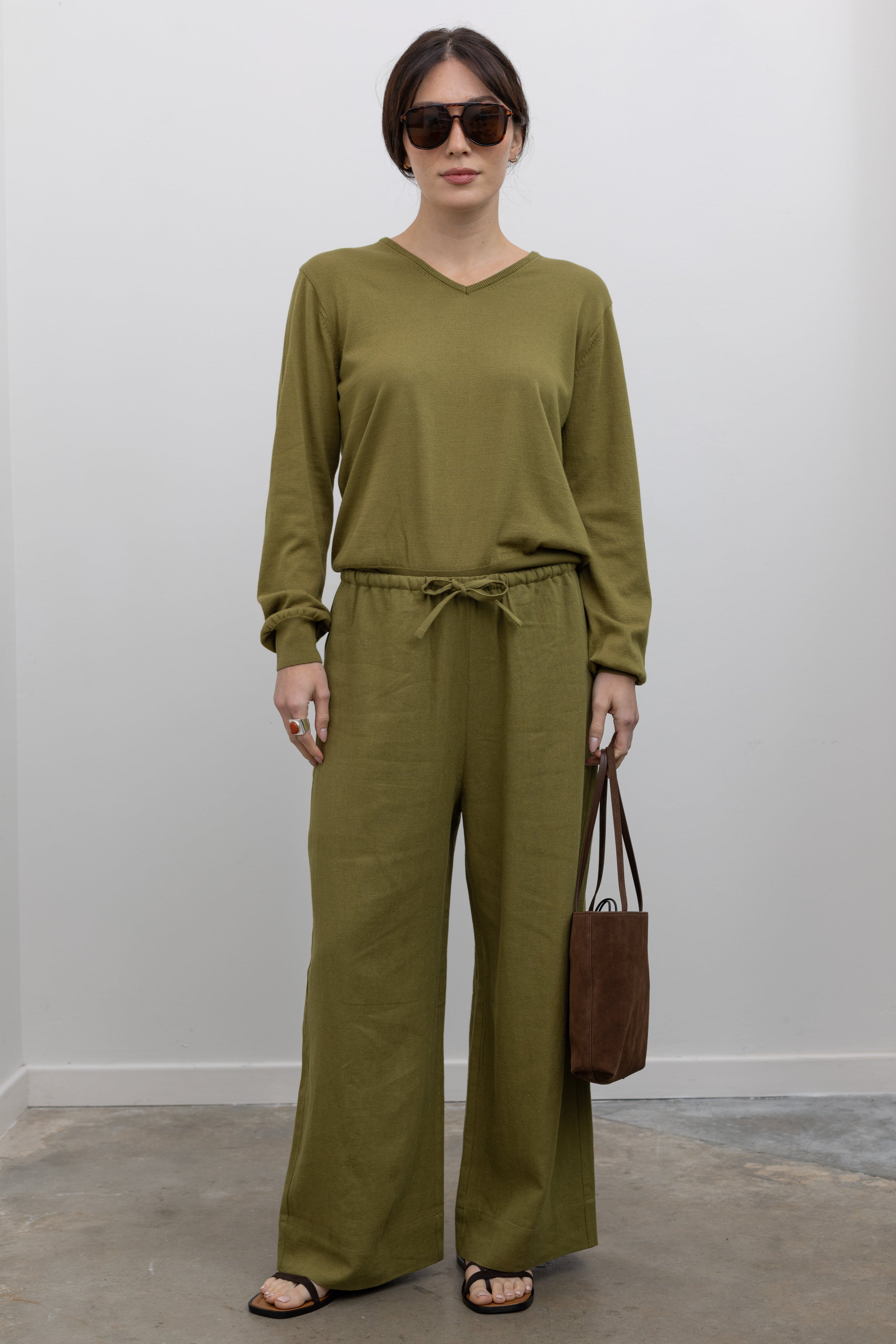 Full length front view of a woman standing wearing elevated casual spring fashion in the Mijeong Park Green Cotton Blend V-Neck Knit Top paired with the Green Linen Blend Wide Leg Cropped Pants featuring a comfortable drawstring waist, front and back patch pockets, and a cropped length suitable for a minimalist, versatile wardrobe at an Alas Eius store. 