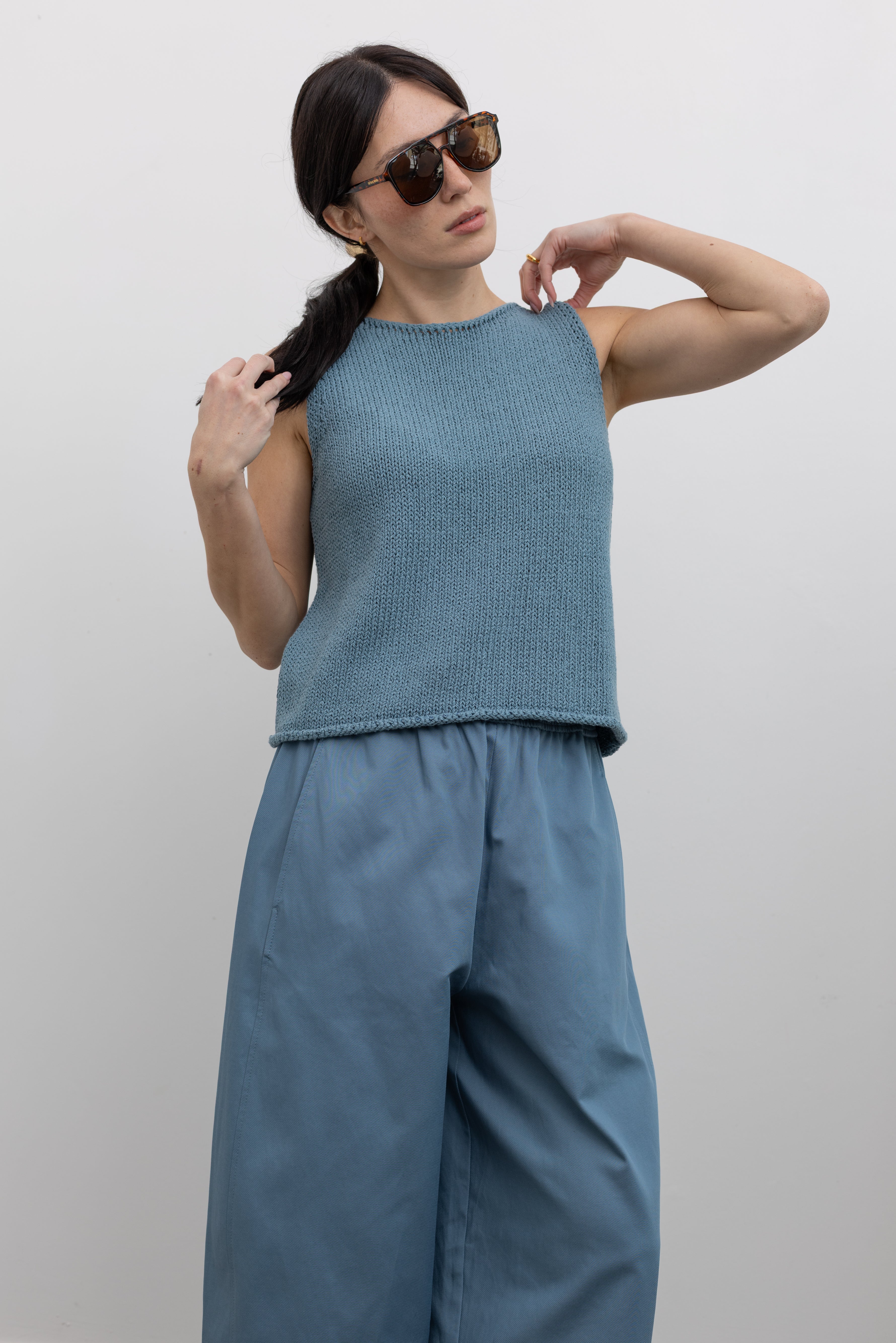 Front view of a woman wearing spring fashion in a Mijeong Park light blue boat neck knit sweater tank top featuring rolled edges around the neckline and hem at an Alas Eius store. 