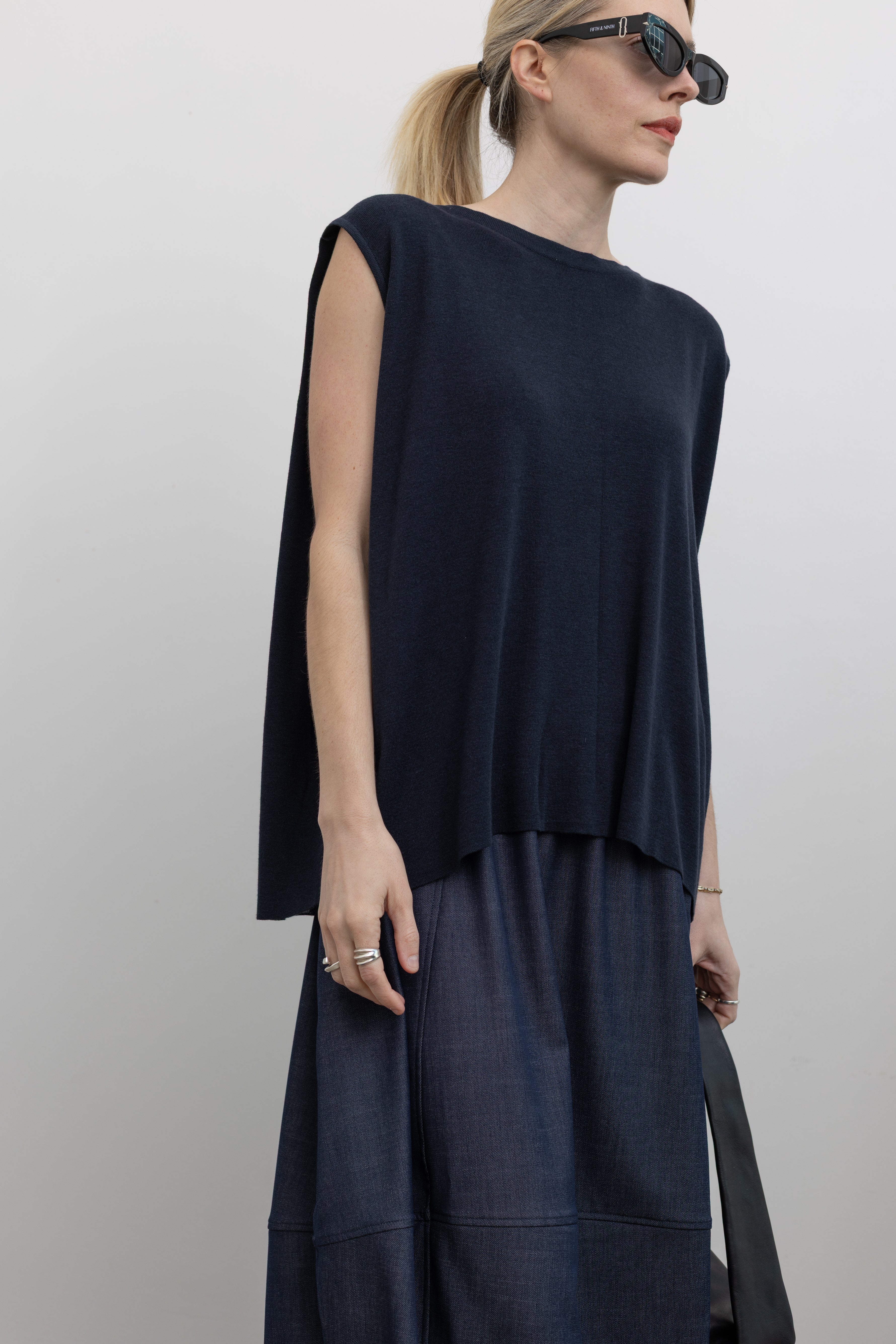 3/4 front view of a woman wearing a Mijeong Park navy blue sleeveless top with a draped back and a curved front hem at an Alas Eius store. 
