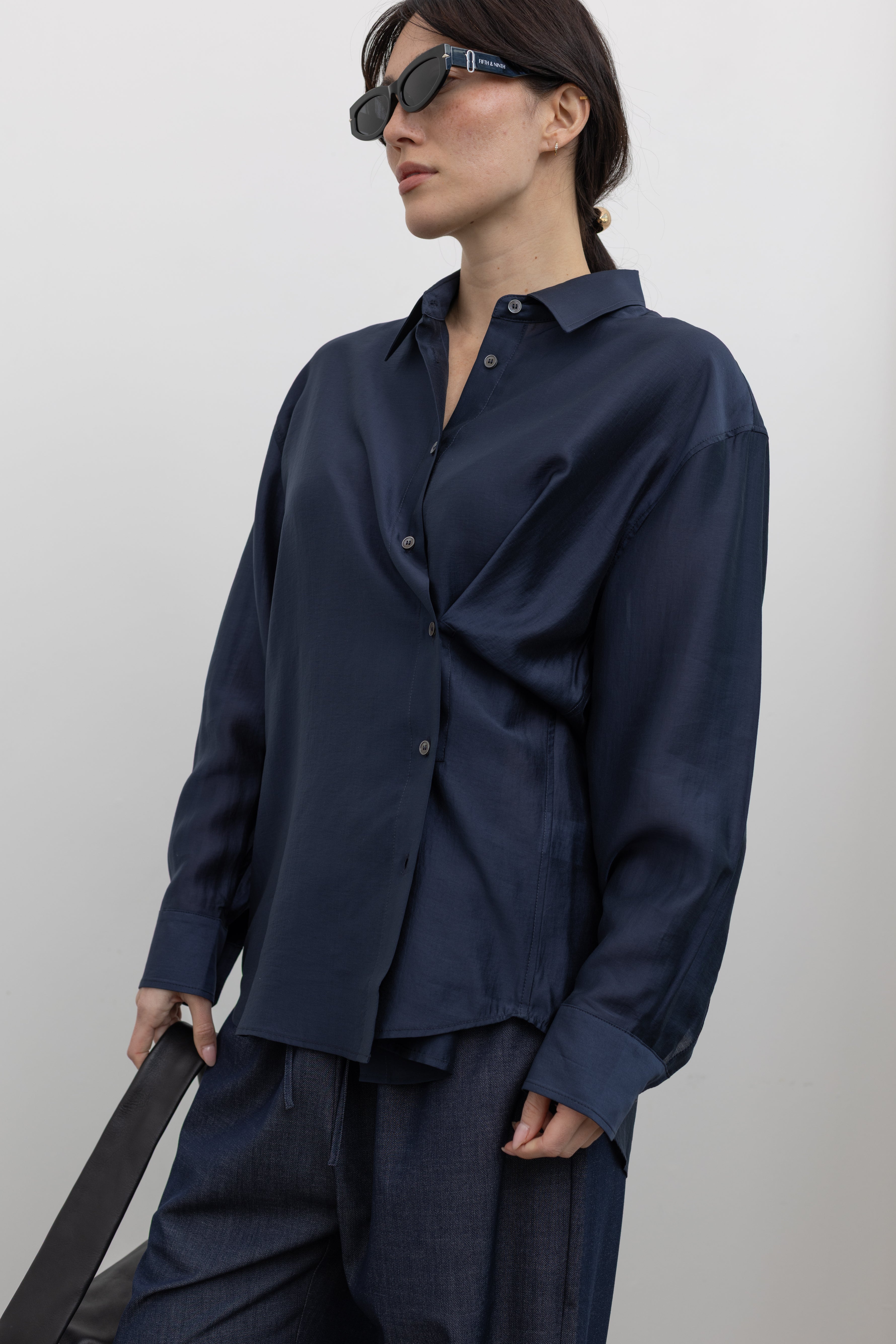 3/4 view of a woman wearing an elevated classic spring staple in a Mijeong Park navy blue semi-sheer oversized shirt featuring a flattering off-center button front, long sleeves, and a classic sharp collar at an Alas Eius store. 