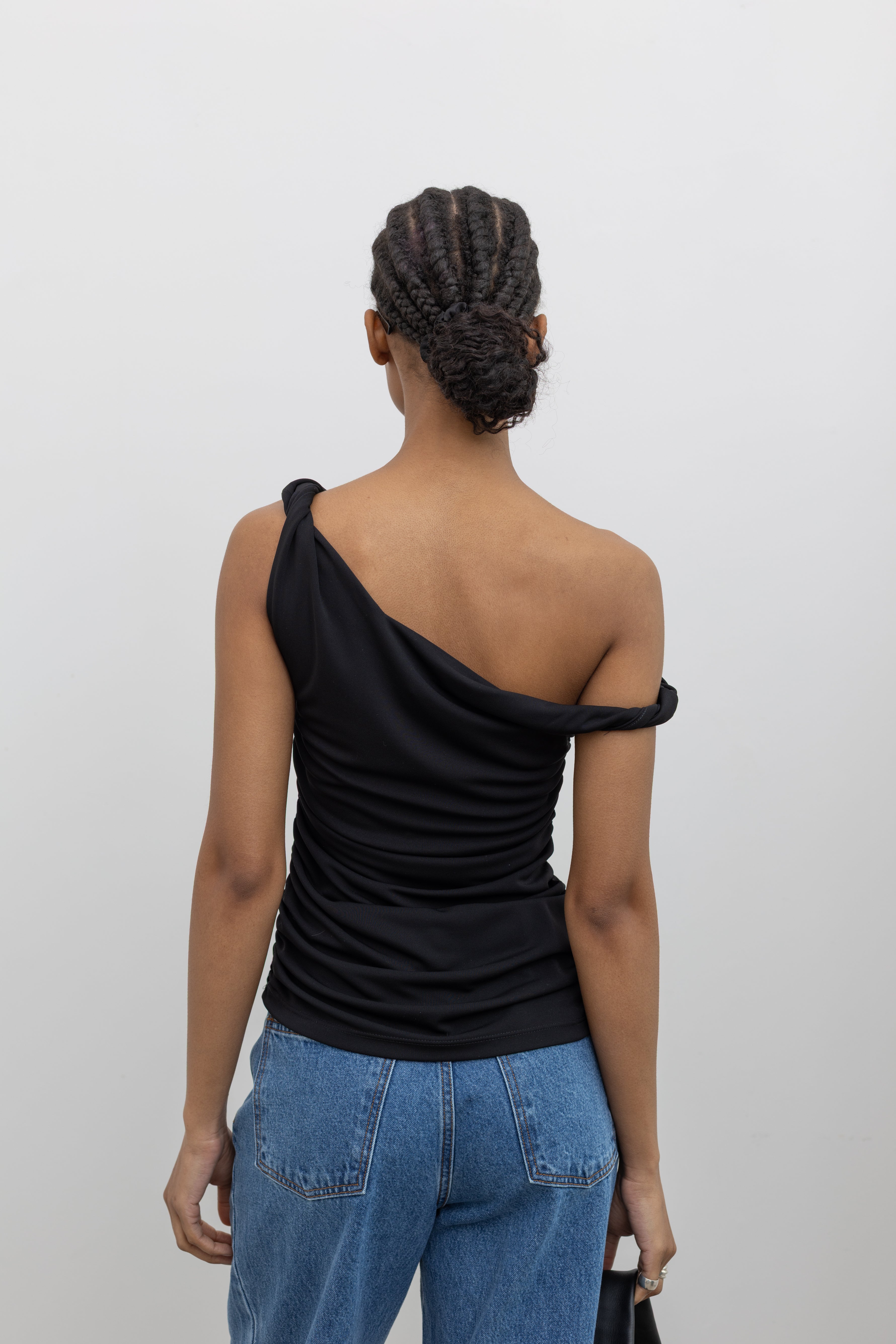 Close-up back view of a woman posing wearing Spring fashion in light wash denim jeans paired with a flattering Nomia black twisted off the shoulder straps and shirring detail on side seams at Alas Eius.