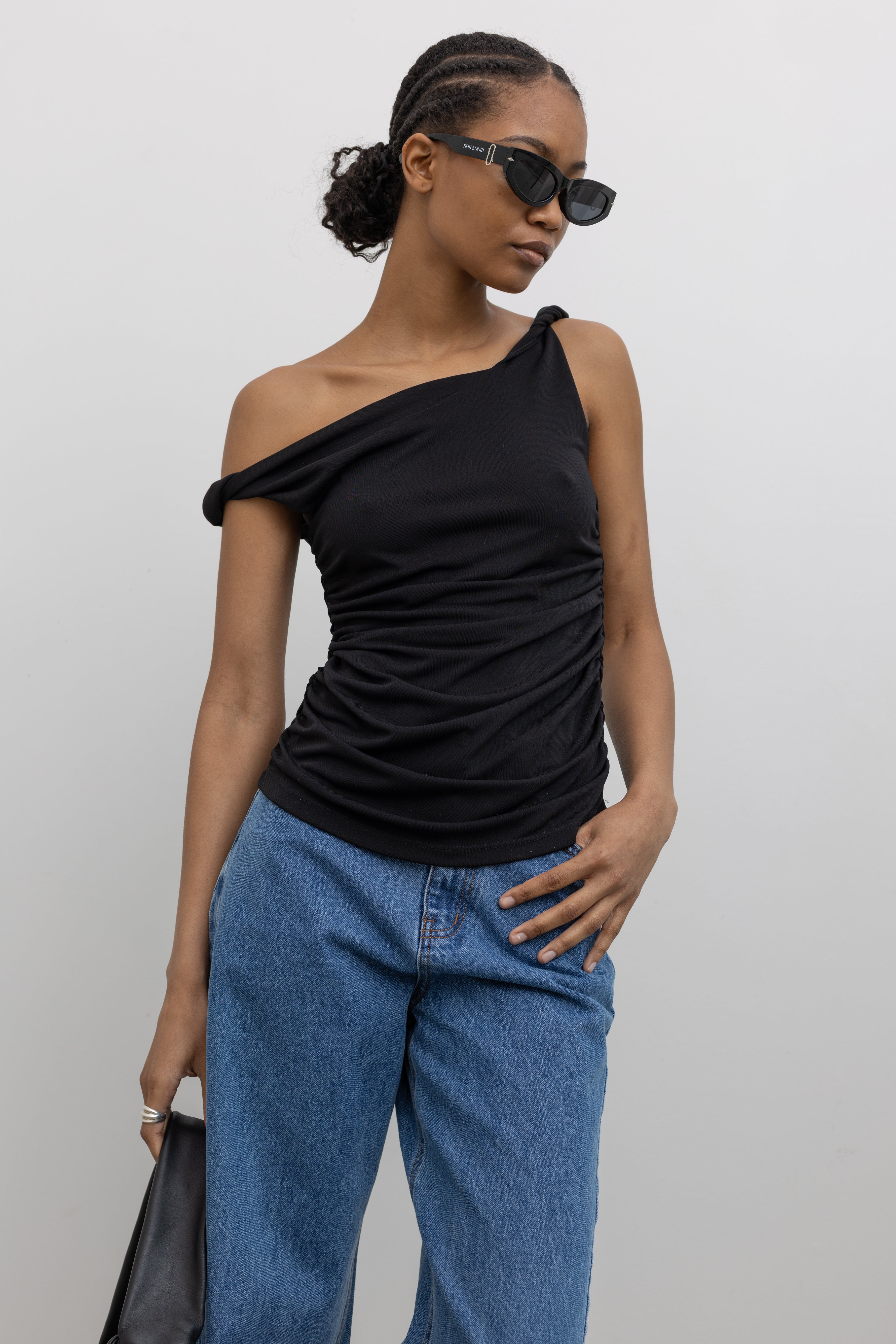 Woman posing wearing Spring fashion in light wash denim jeans paired with a flattering Nomia black twisted off the shoulder straps and shirring detail on side seams at Alas Eius.
