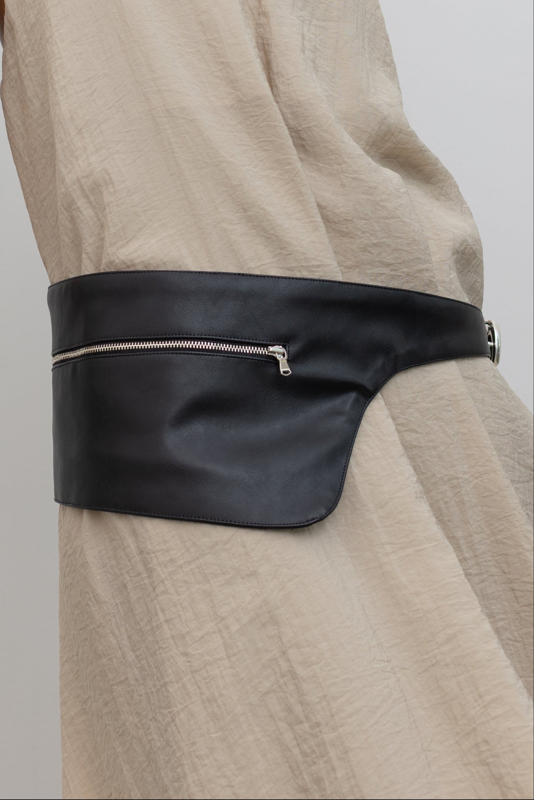 Woman wearing modern minimalist Nomia faux leather black belt bag with zip pocket and puffy spiral silver hardware at an Alas Eius store. 