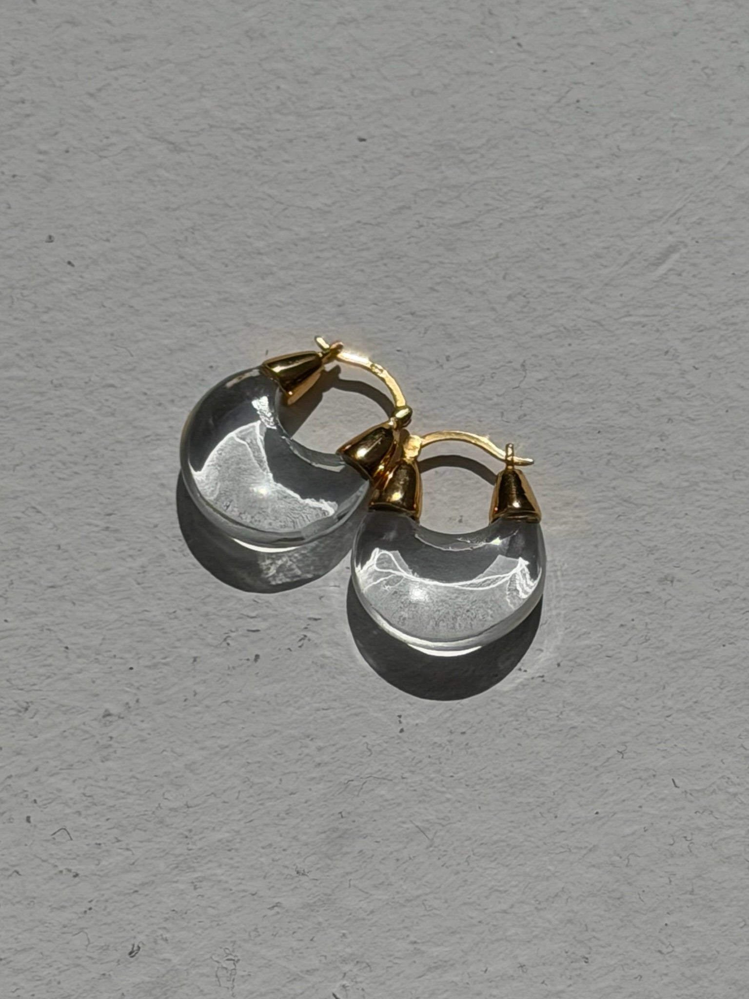 Product view of modern contemporary Nomia clear carved tear drop hoop crystal earrings with gold vermeil hinge at an Alas Eius store.