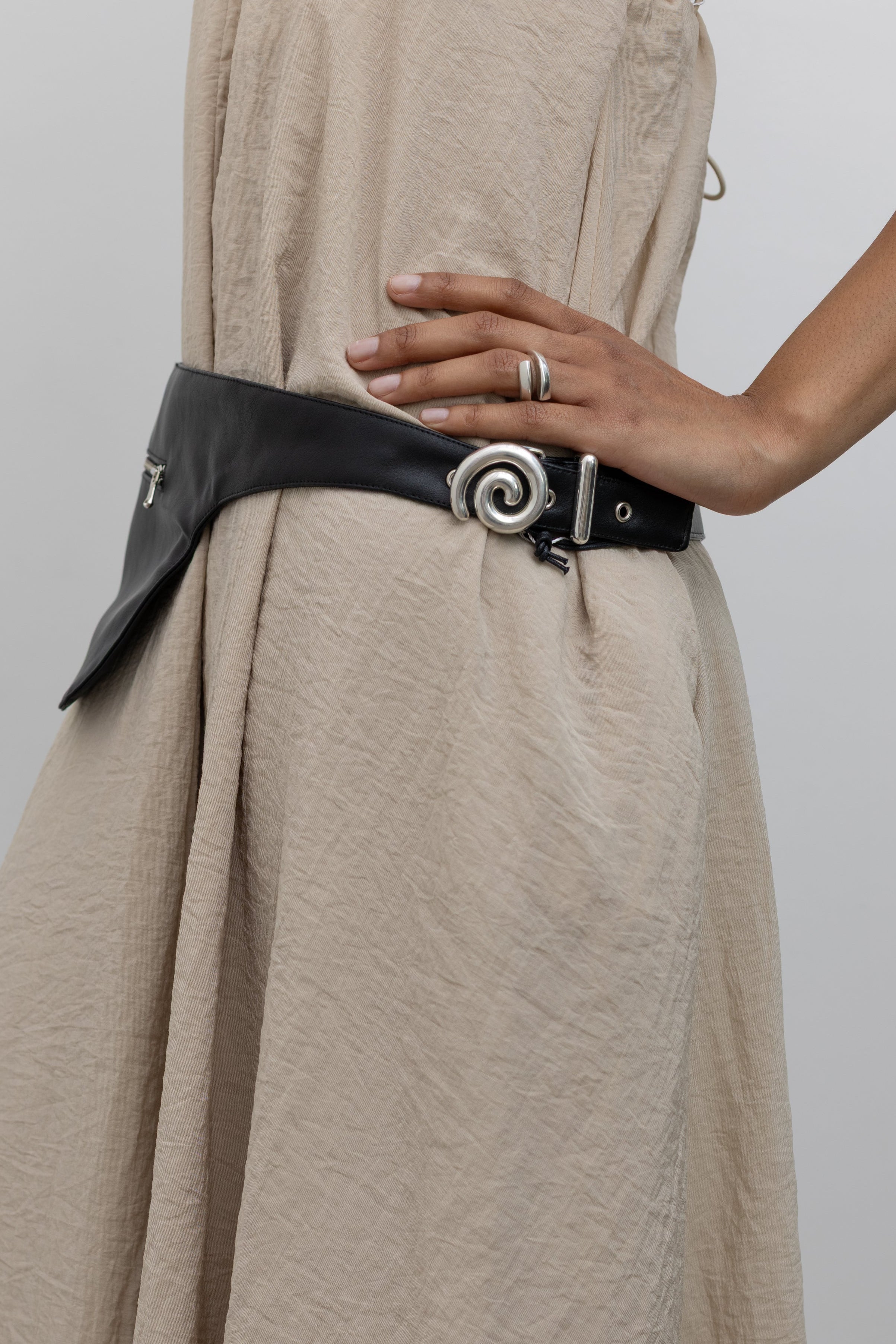 Woman wearing modern minimalist Nomia faux leather black belt bag with zip pocket and puffy spiral silver hardware at an Alas Eius store. 