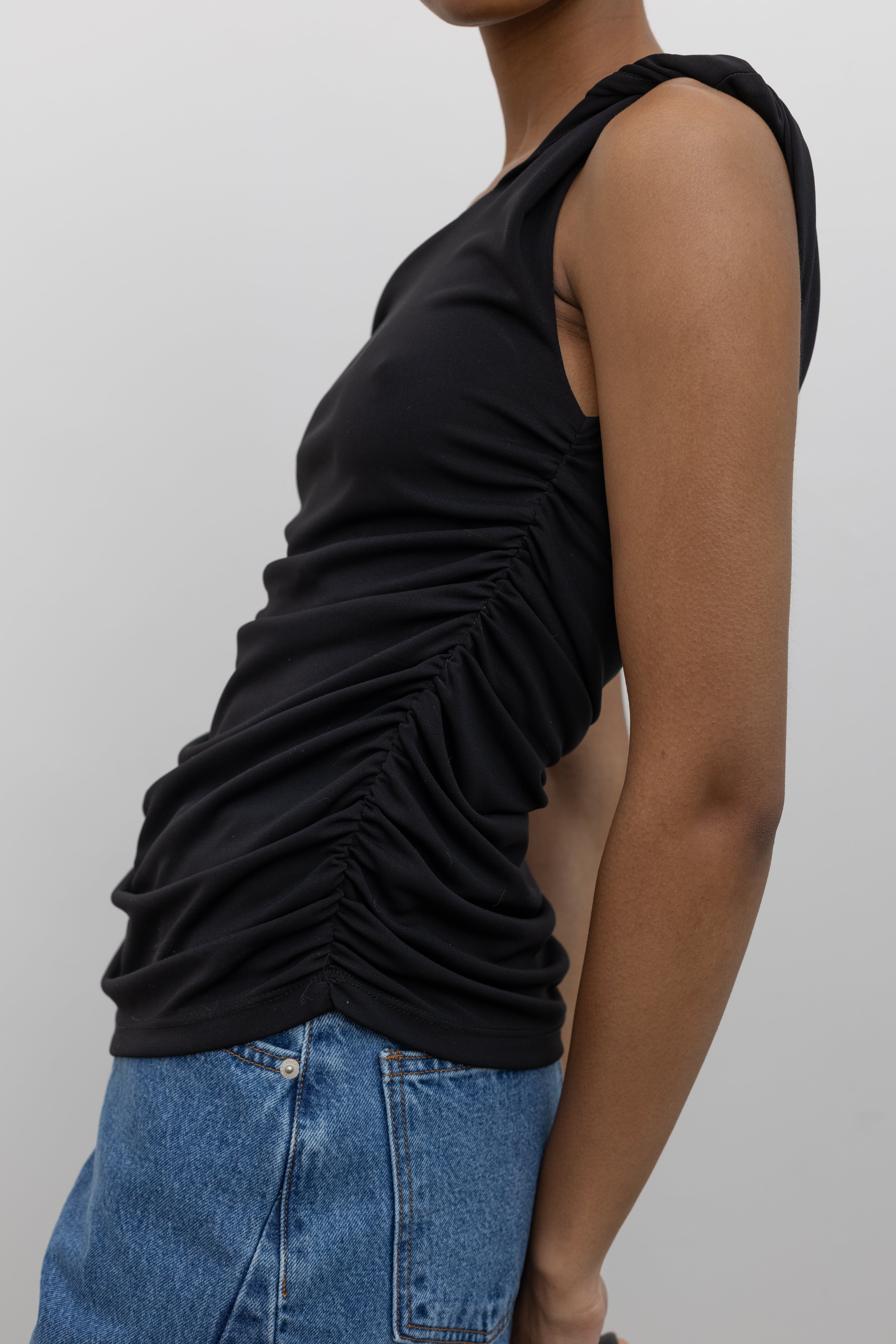 Woman posing wearing Spring fashion in light wash denim jeans paired with a flattering Nomia black twisted off the shoulder straps and gathered detail on side seams at Alas Eius.