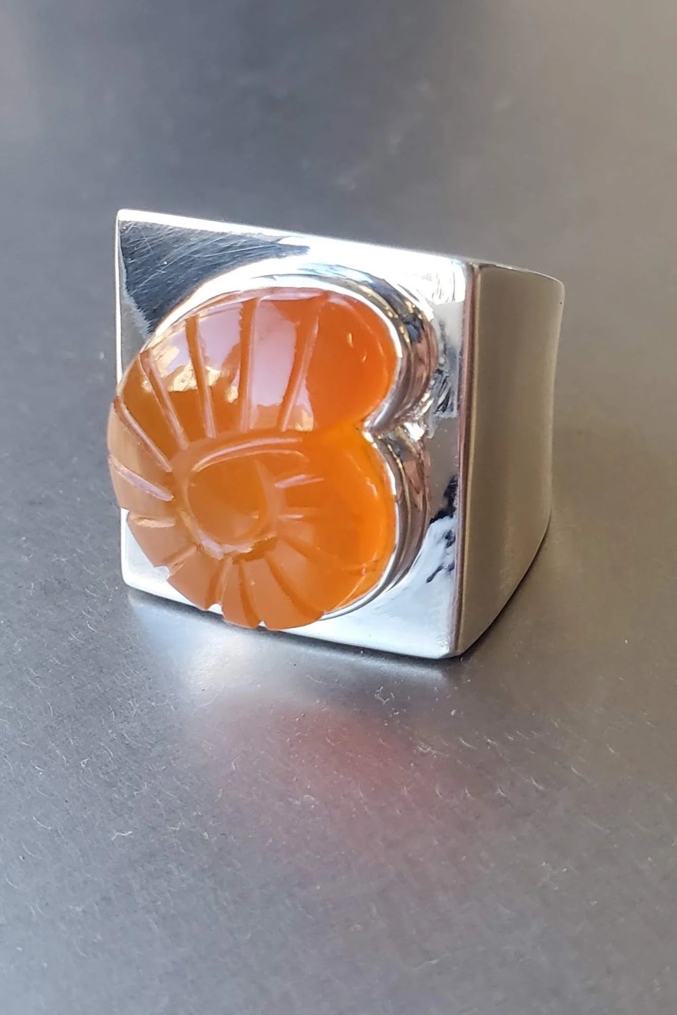 Close-up product view of contemporary design in a Nomia statement ring crafted in high polished solid sterling silver with a red hand carved Nautilus Stone design at an Alas Eius store.