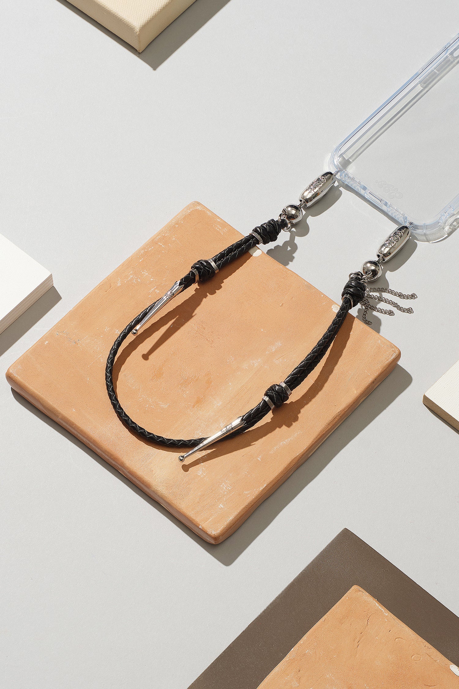 Black braided cord keychain on a beige square block with a clear plastic case in the background. Ossa New York at Alas Eius