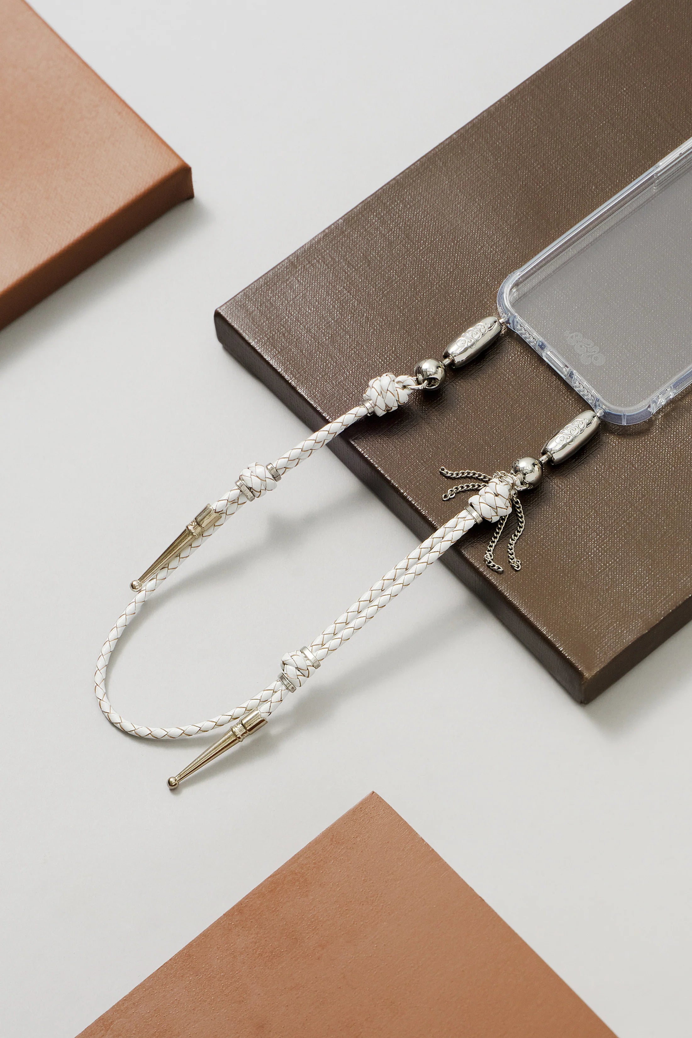 Silver beaded lanyard on a clear phone case with a brown and white geometric background. Ossa New York at Alas Eius